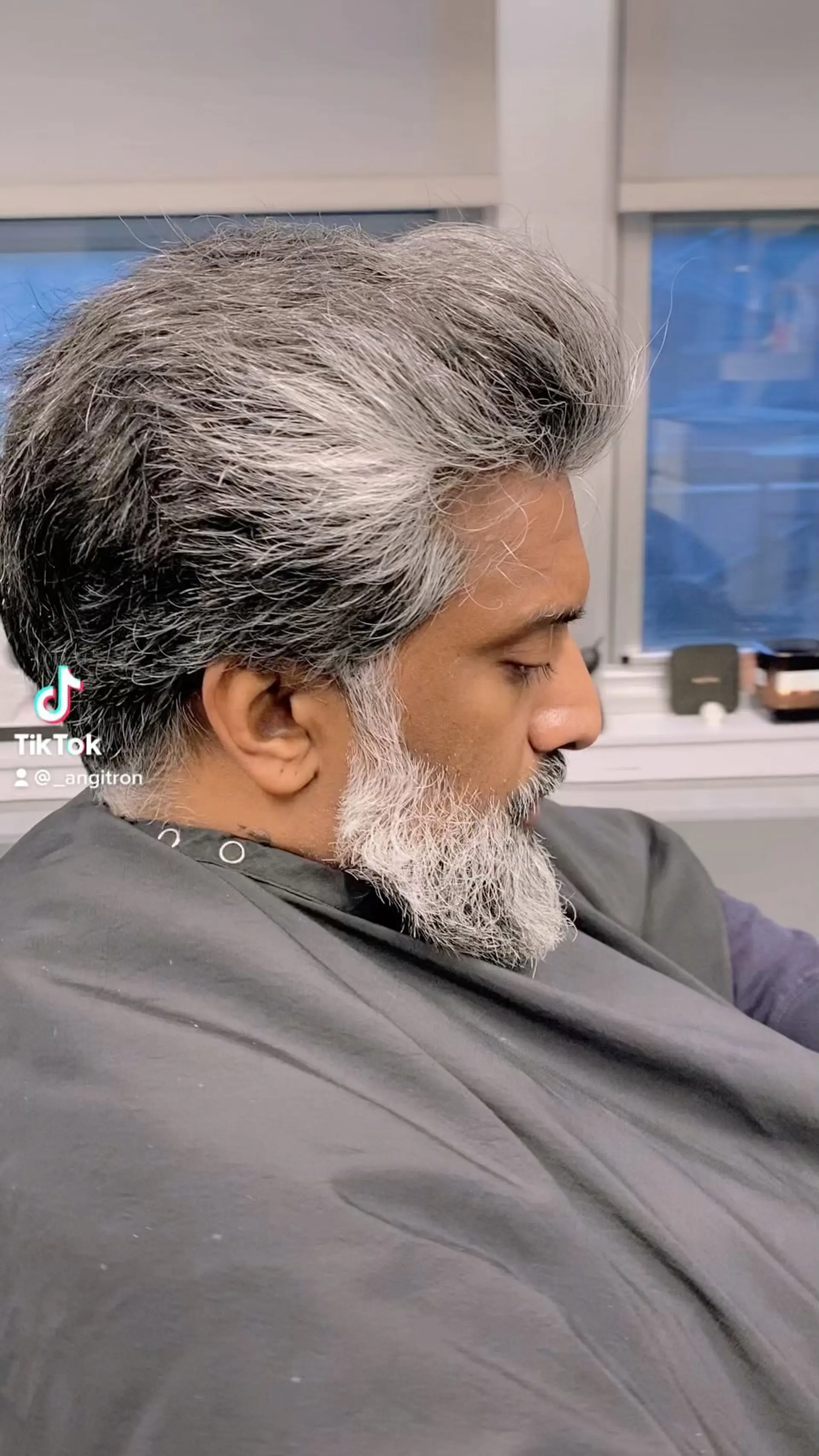 A textured, voluminous men's swept-back haircut featuring natural salt-and-pepper hair paired with a defined beard. 1