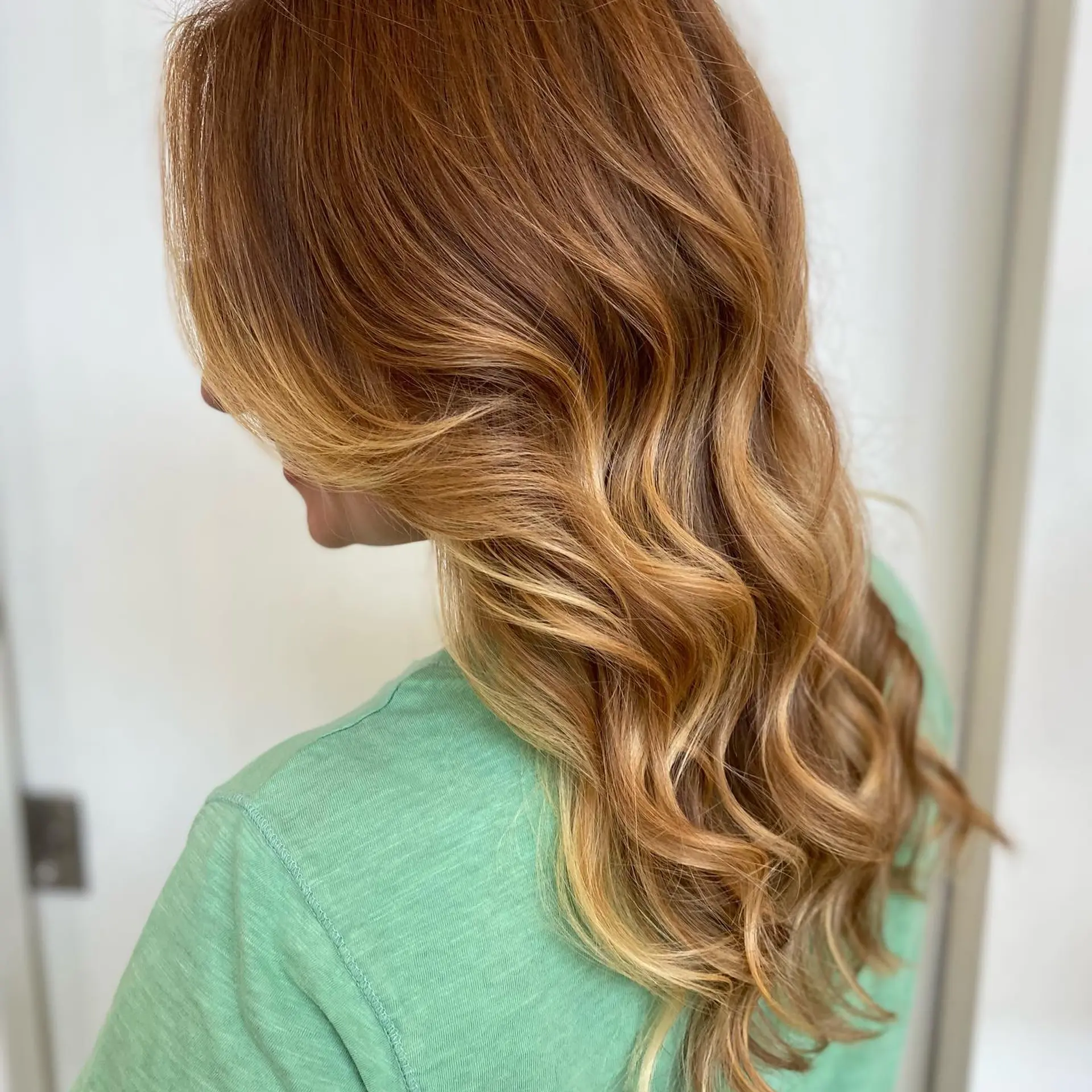 Warm copper-auburn hair seamlessly transitioning into honey blonde balayage highlights, styled into soft cascading waves. 1