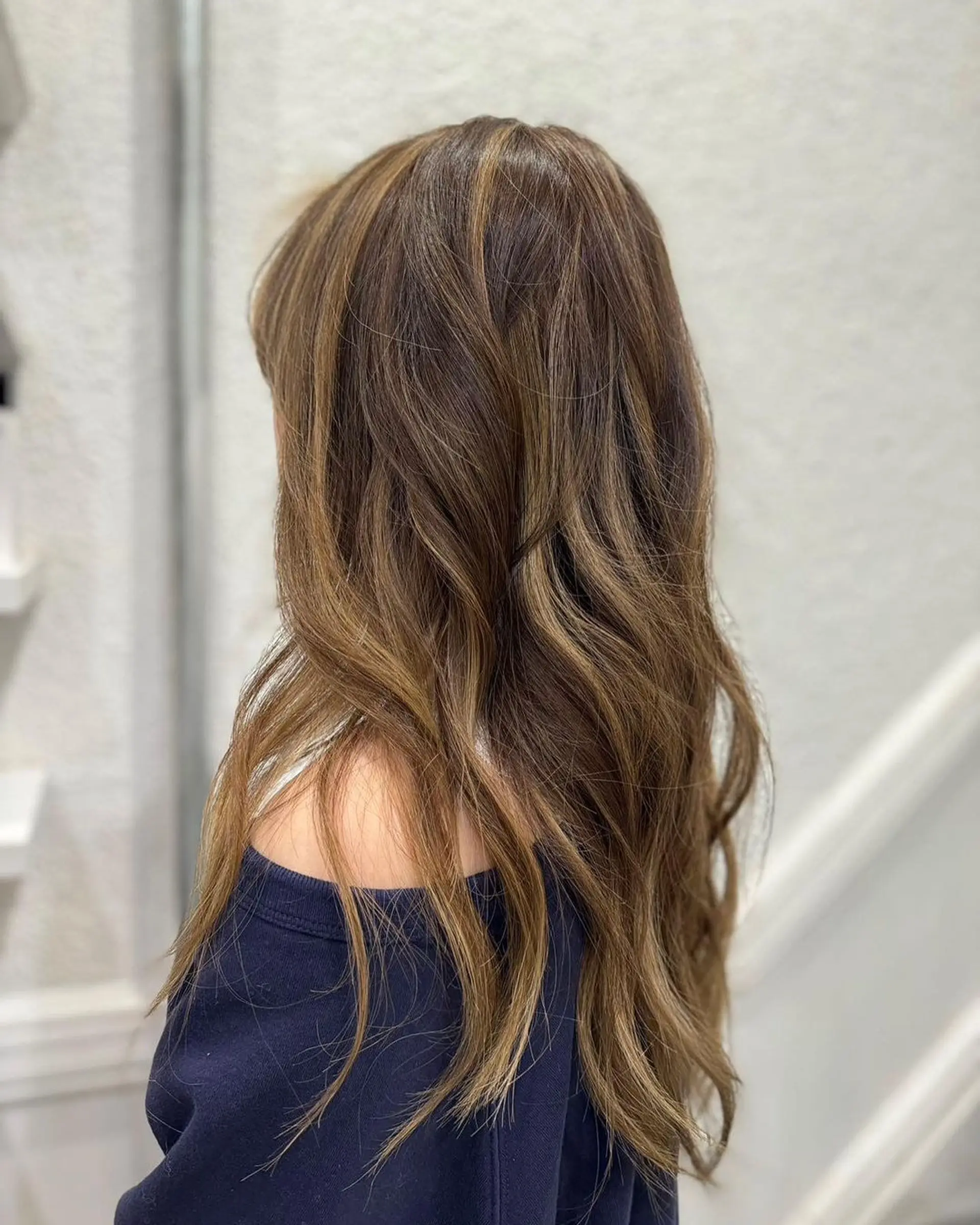 Long, wavy hair with a rich brown color, accented with natural blonde highlights. The waves are softly tousled, creating a beachy, effortless look with layered volume and movement. 1
