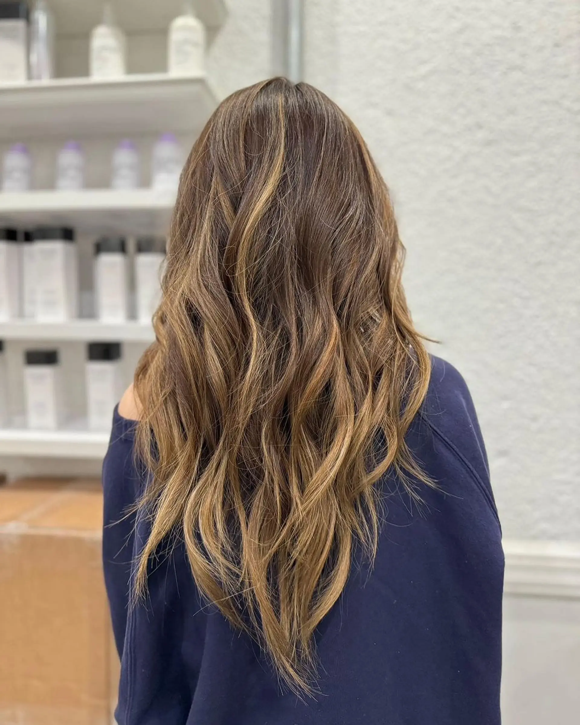 Long, wavy hair with a rich brown color, accented with natural blonde highlights. The waves are softly tousled, creating a beachy, effortless look with layered volume and movement. 2