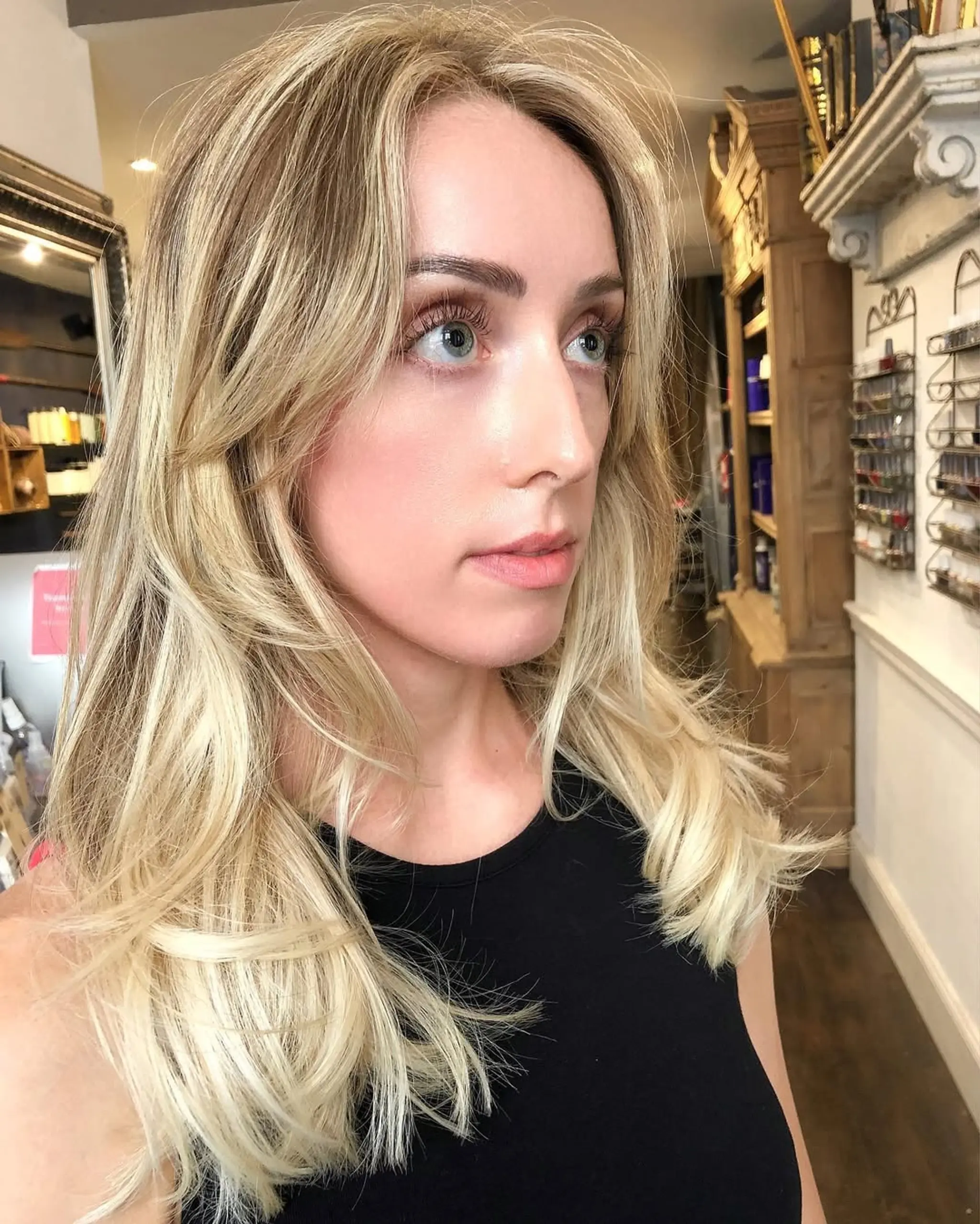 Medium-length, wavy, layered hairstyle with a blend of blonde and ash tones, middle-parted and face-framing.