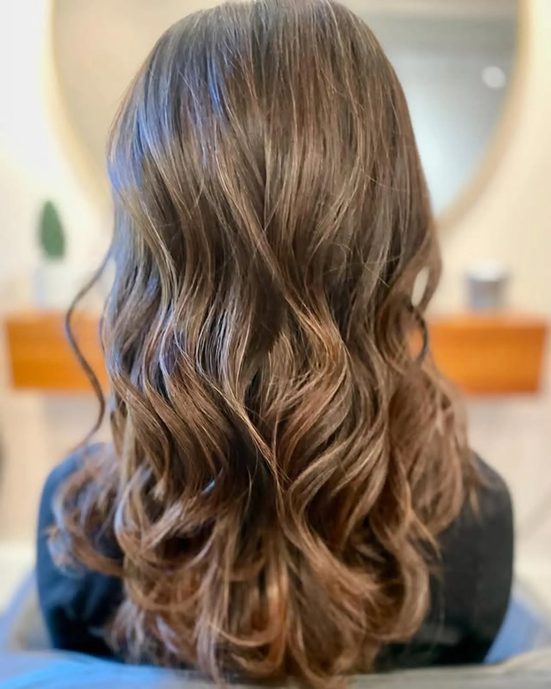 Medium-length hair styled with soft, cascading waves and subtle, dimensional balayage highlights in caramel and light brown tones. 1
