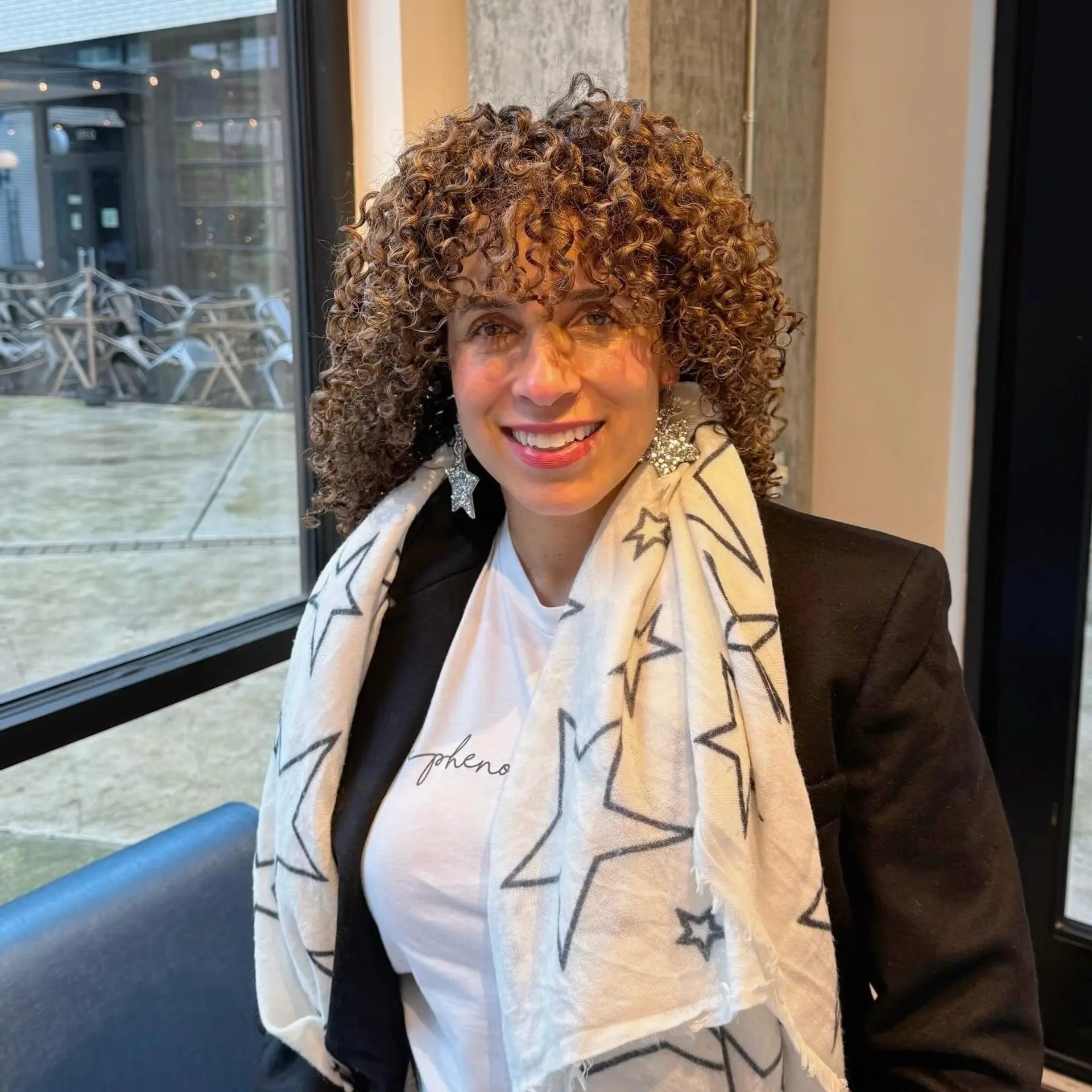Shoulder-length defined curls cut with rounded volume, a full curly fringe, and dimensional caramel balayage highlights. 1
