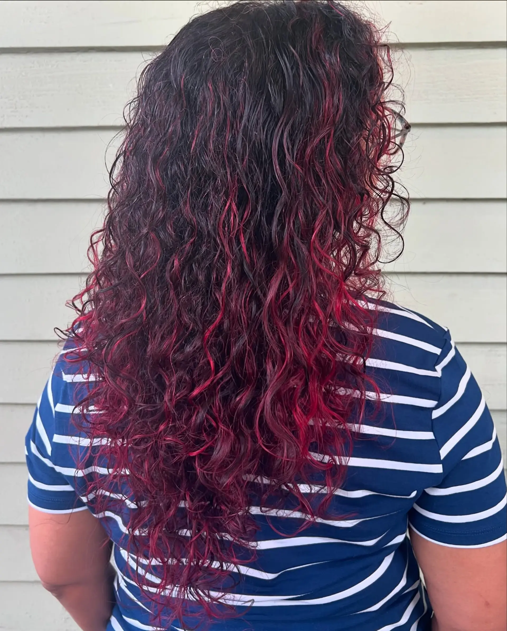 Long curly hair styled with a vivid cherry red or magenta balayage, featuring a deep, dark root that transitions into bright, playful curls for a dynamic and textured look. 2