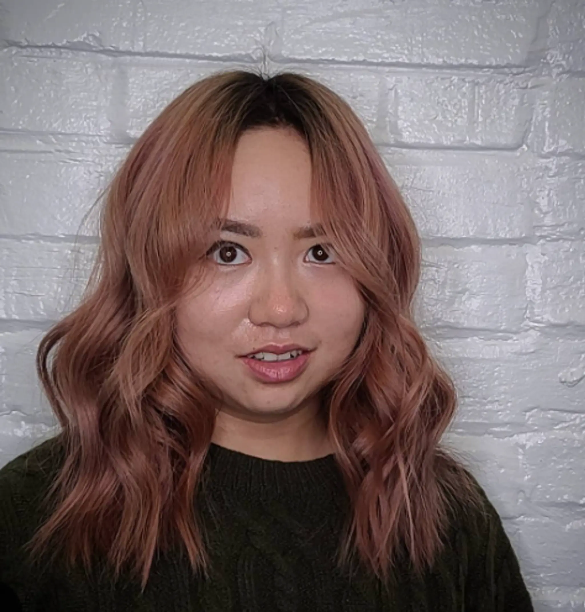 Medium-length, wavy rose gold hair with pink and copper undertones. Features soft waves, a middle part, blended highlights, and face-framing layers.