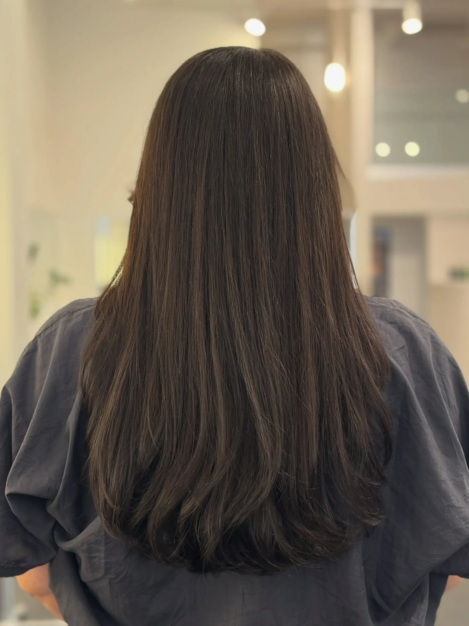 A sleek, long dark brunette haircut styled with soft, curved layers through the ends for natural movement and volume. 1