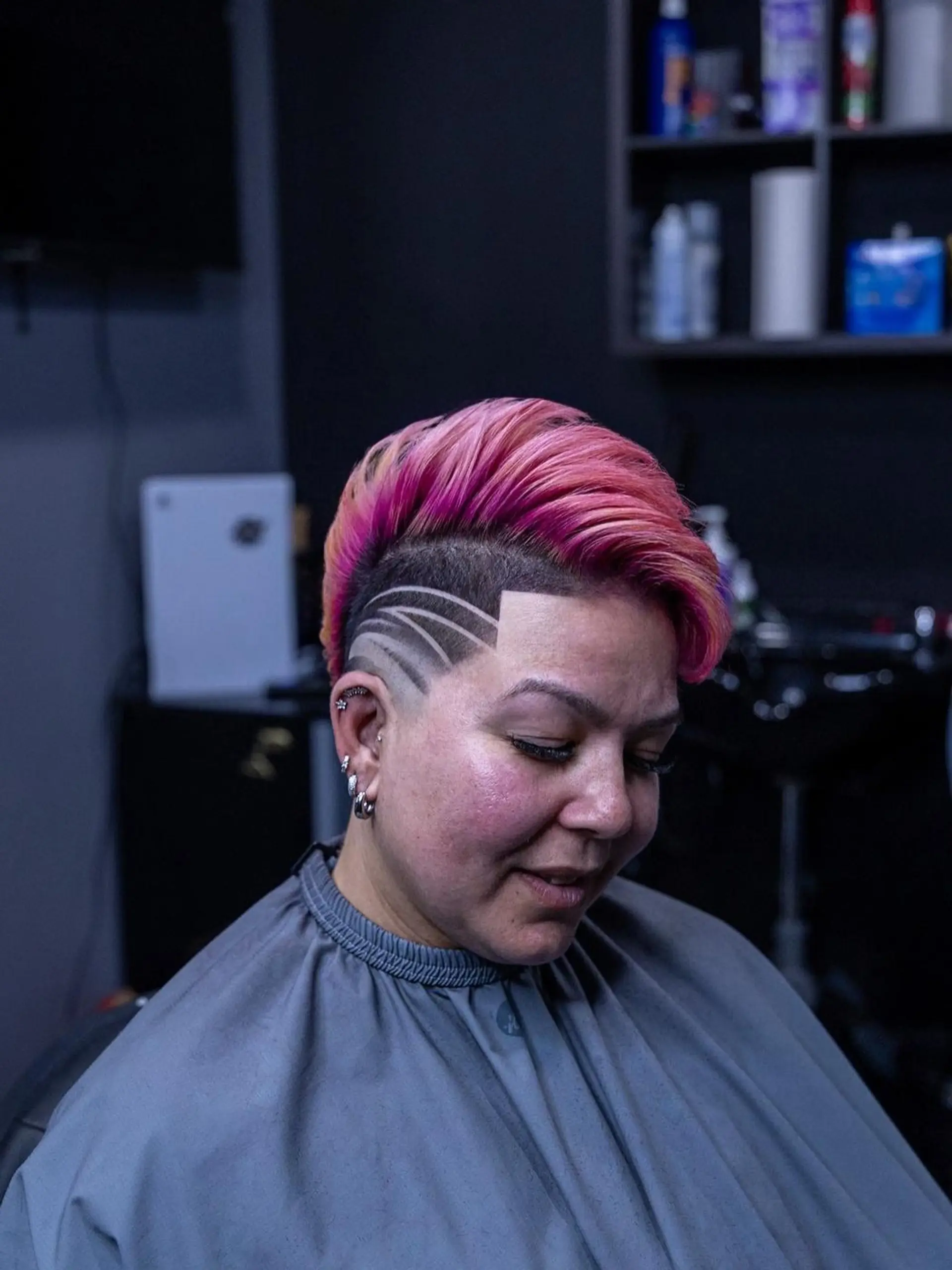 A bold short undercut featuring textured pink and magenta hair on top with sharp curved line designs etched into the faded sides. 1