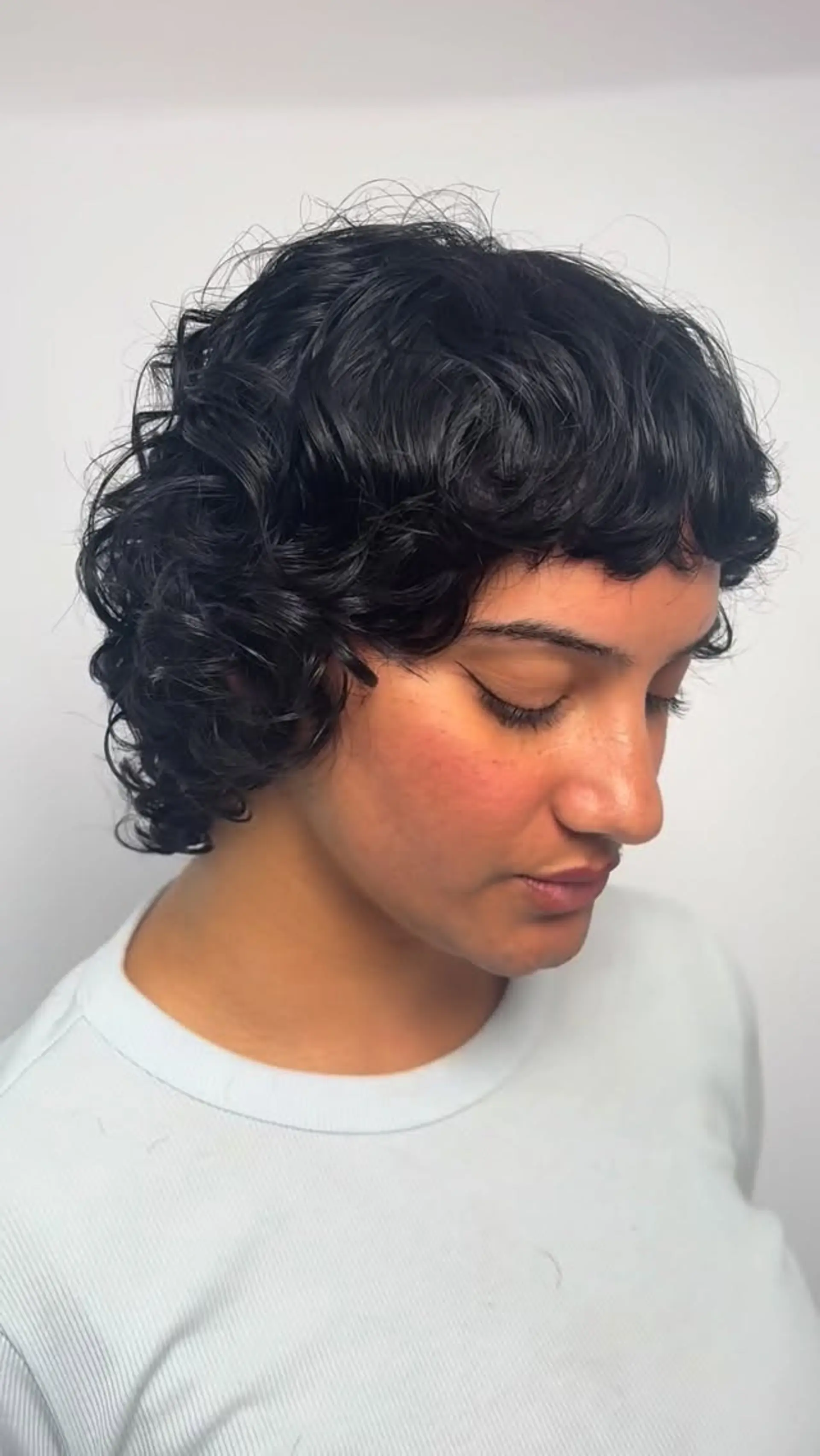 A textured short cut with glossy curls, soft ear-skimming layers, and cropped micro bangs. 1