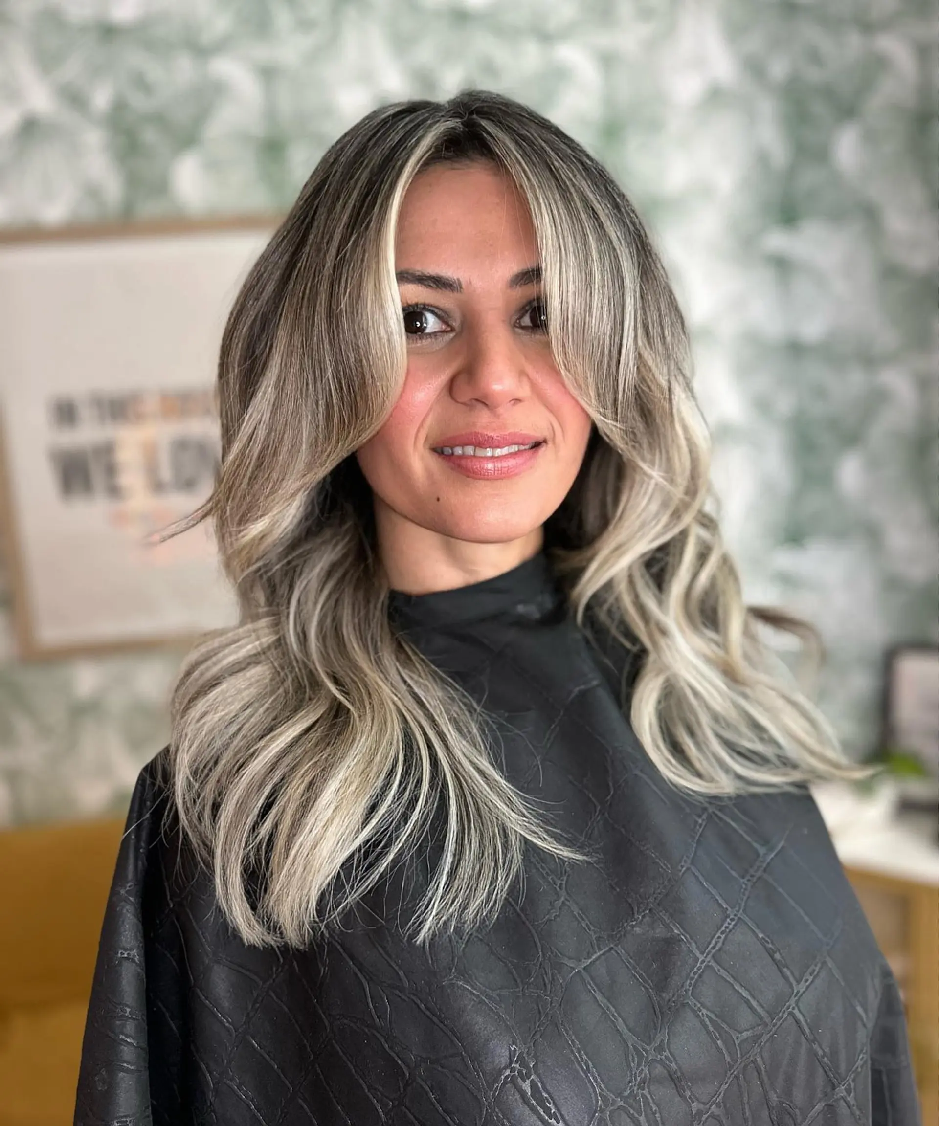 Medium-length ash blonde balayage styled with soft, voluminous waves and face-framing curtain bangs. 1