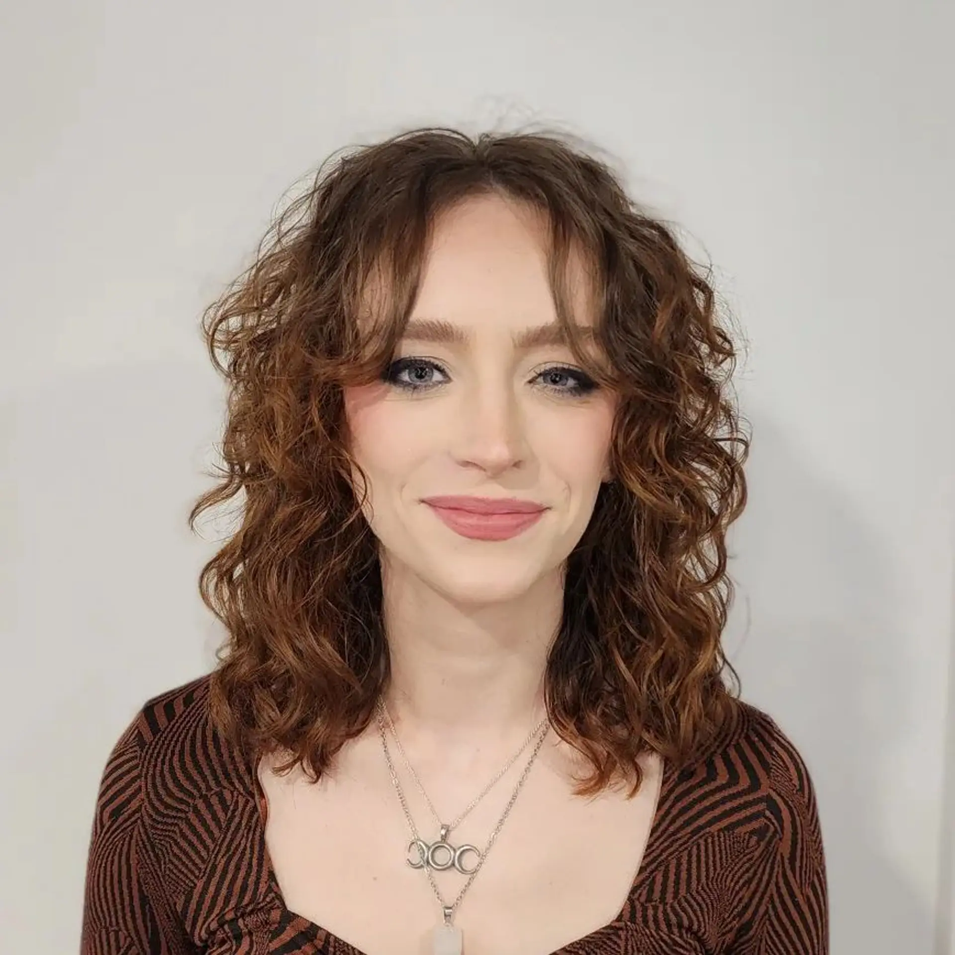 Medium-length chestnut to auburn curly hair with loosely defined curls and natural waves, providing textured volume and a rustic hue. 1