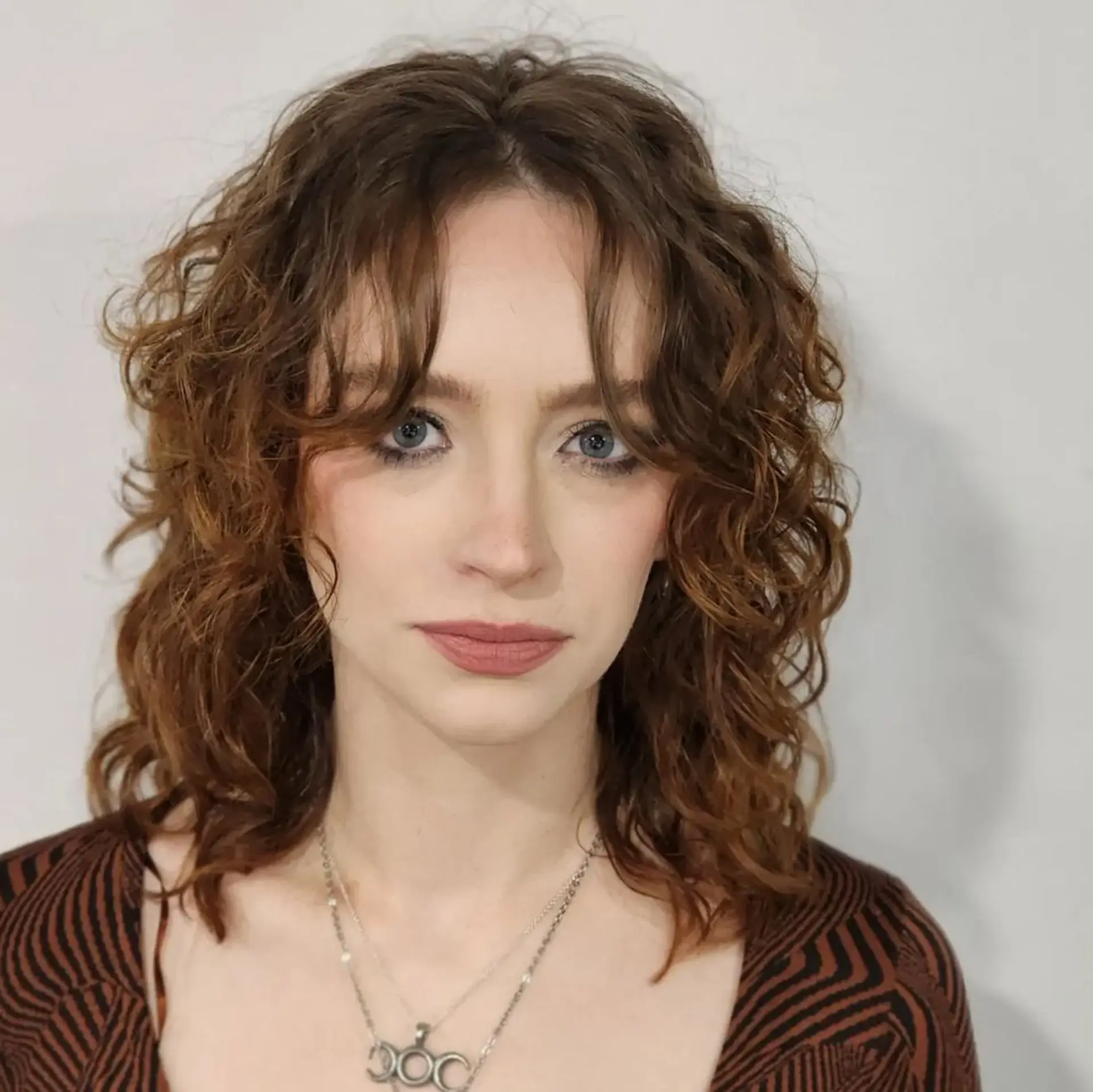 Medium-length chestnut to auburn curly hair with loosely defined curls and natural waves, providing textured volume and a rustic hue. 3