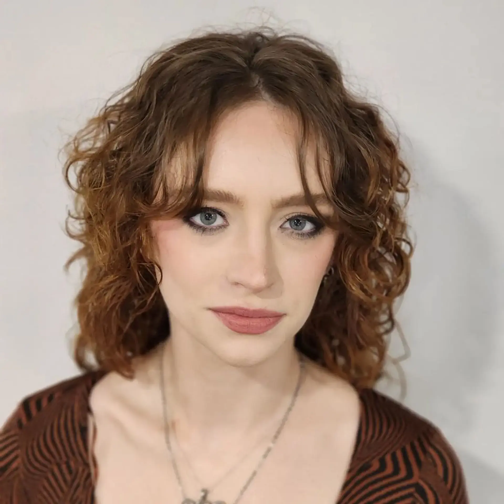 Medium-length chestnut to auburn curly hair with loosely defined curls and natural waves, providing textured volume and a rustic hue. 4