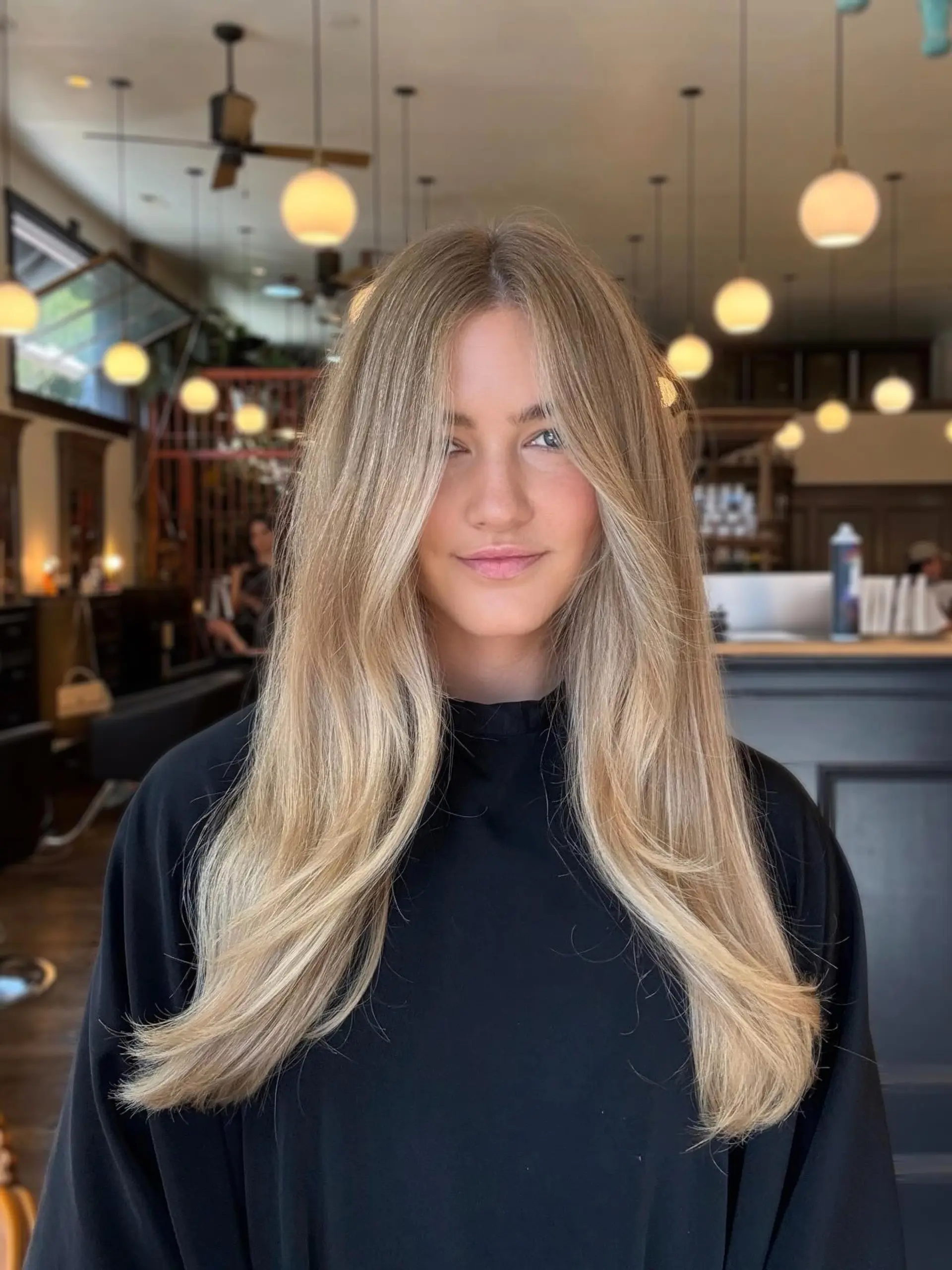 Long lived-in blonde hair styled smooth with a center part and soft, face-framing curtain layers curving naturally outward. 1