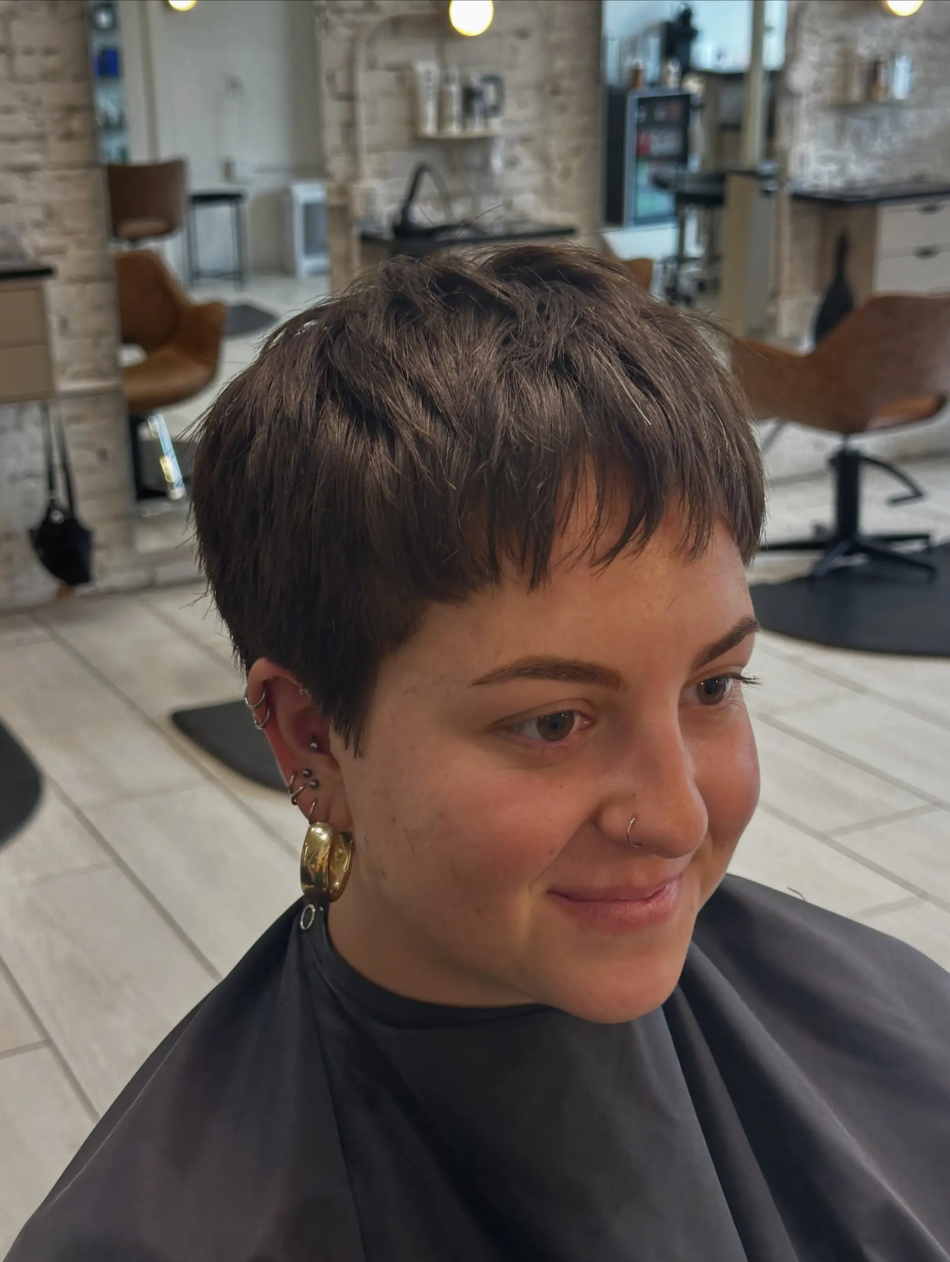 A textured brunette pixie haircut featuring choppy layers and micro fringe bangs framing the forehead. 1
