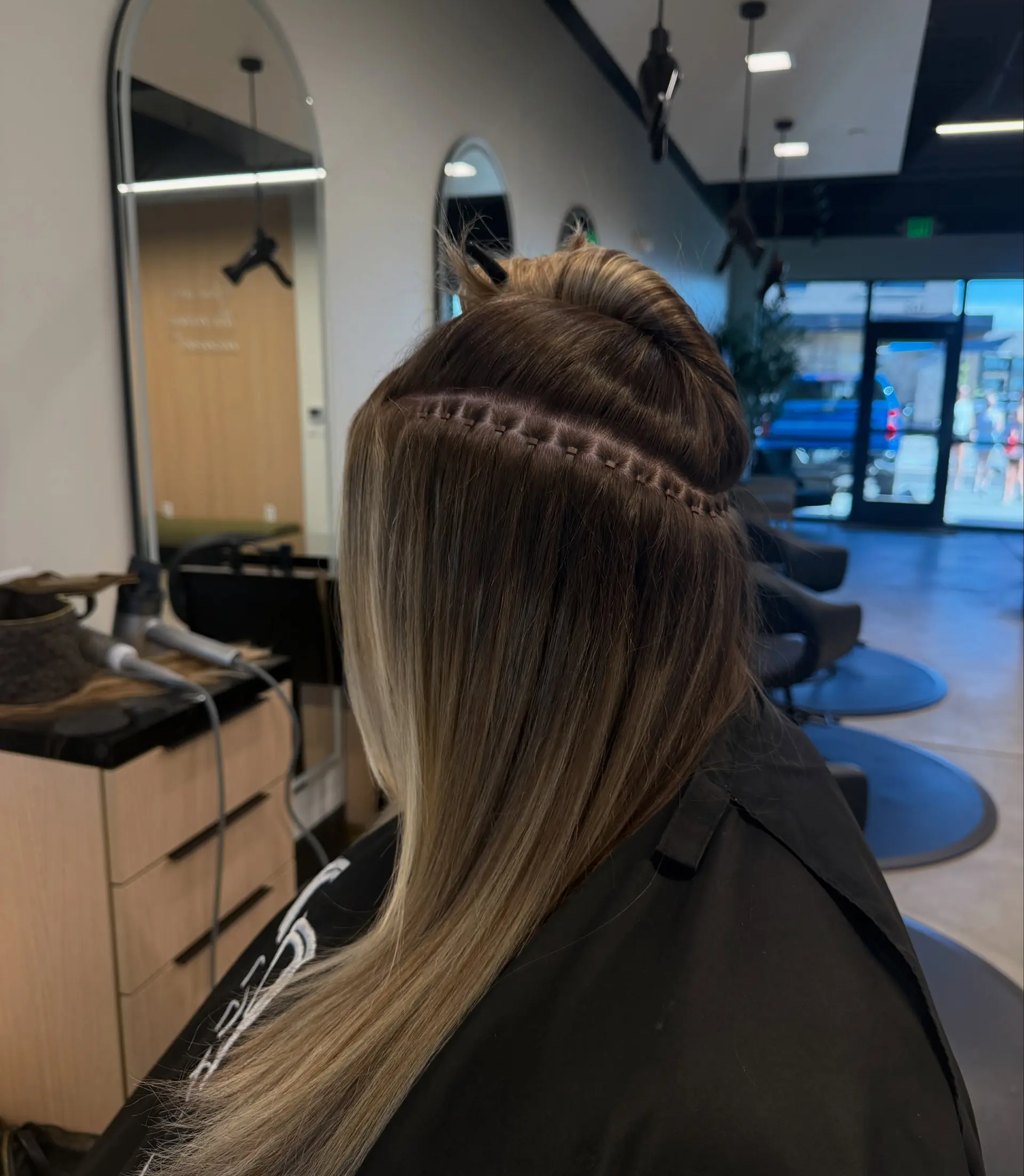 A precise hand-tied weft extension installation shown with the top section clipped up to display the clean stitching and straight blonde-brown hair. 1