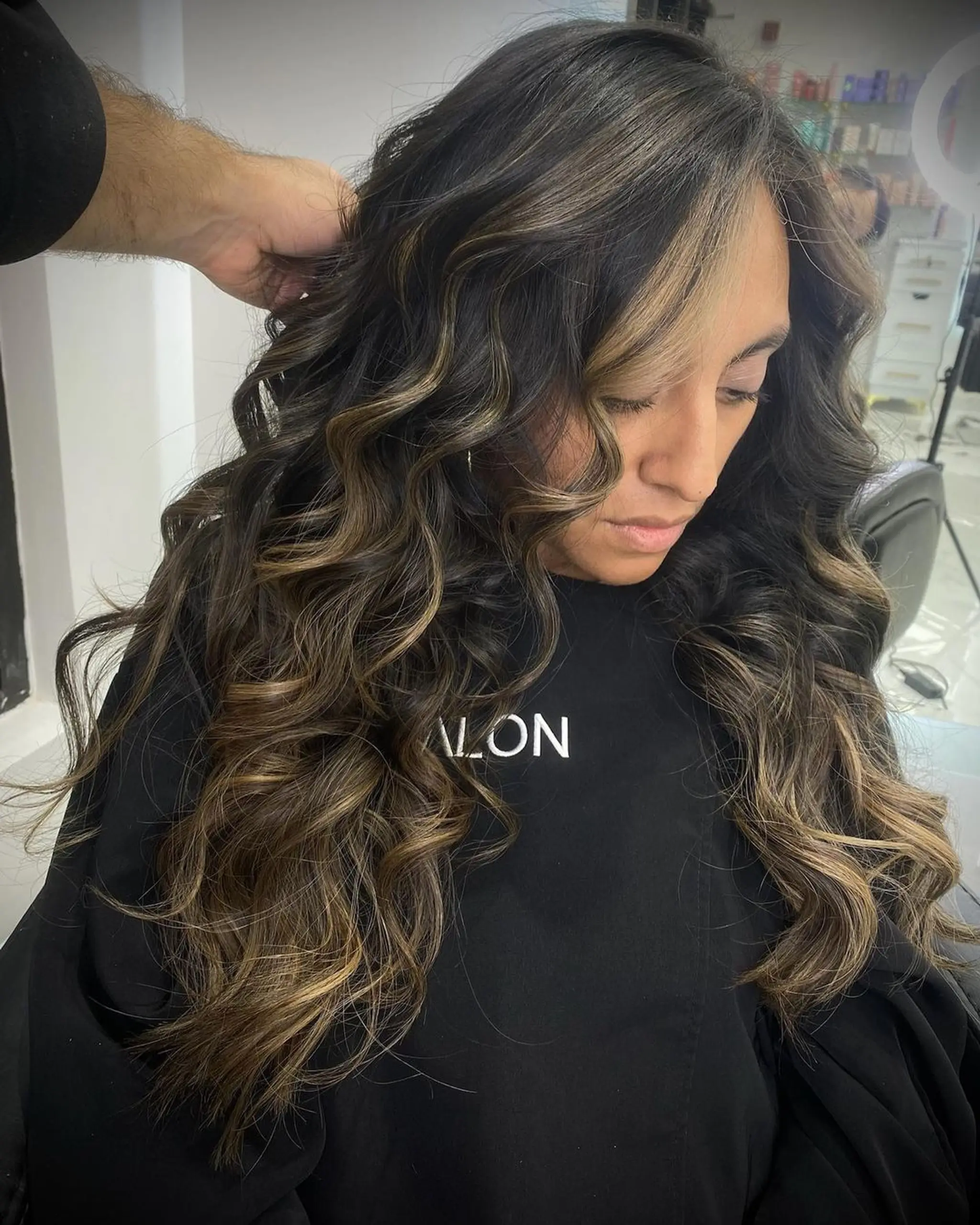 Luxurious long wavy hairstyle with black hair and golden brown highlights, featuring soft, cascading curls.