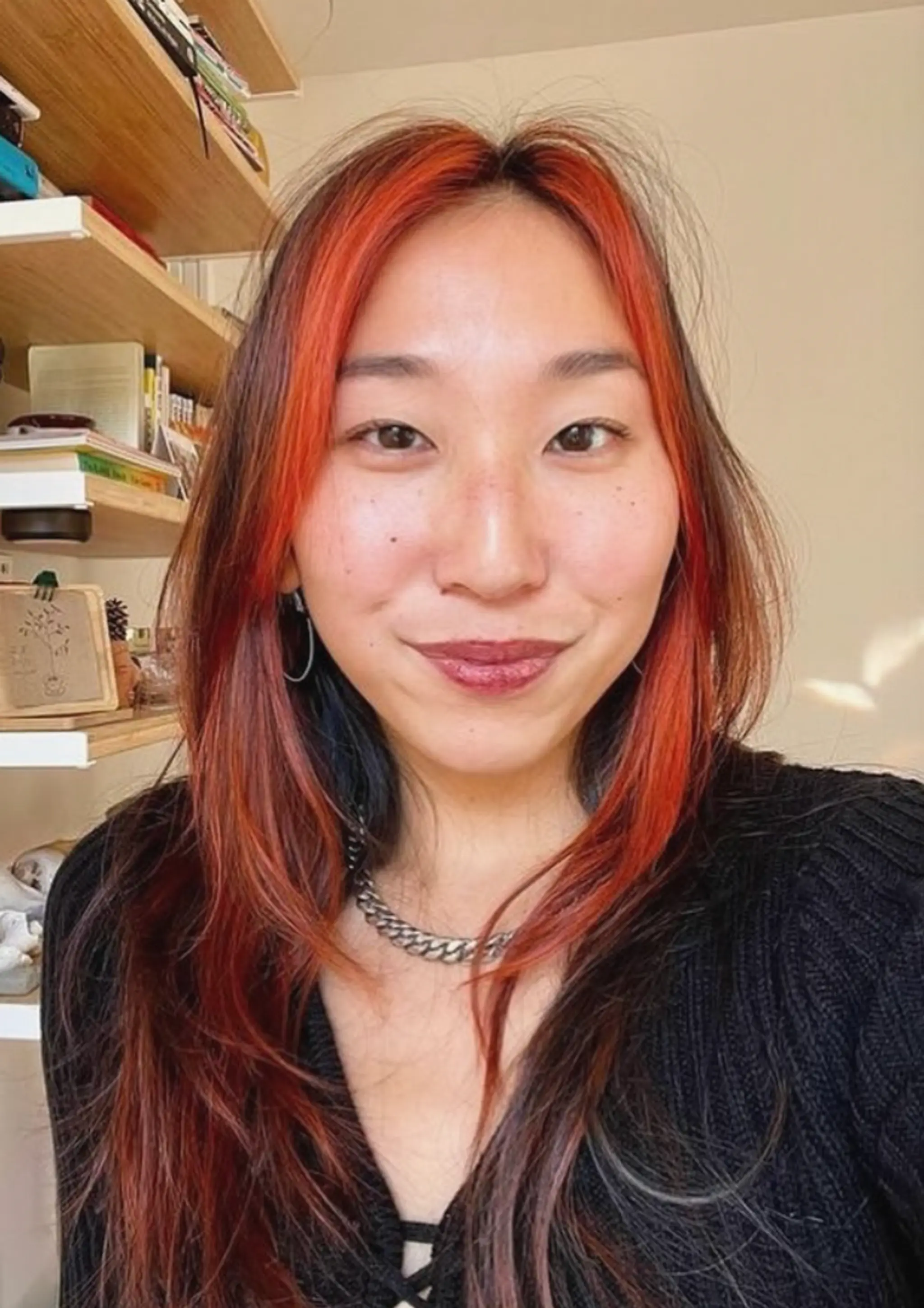 Long, wavy hair with vibrant red highlights, face-framing layers, and natural black roots.