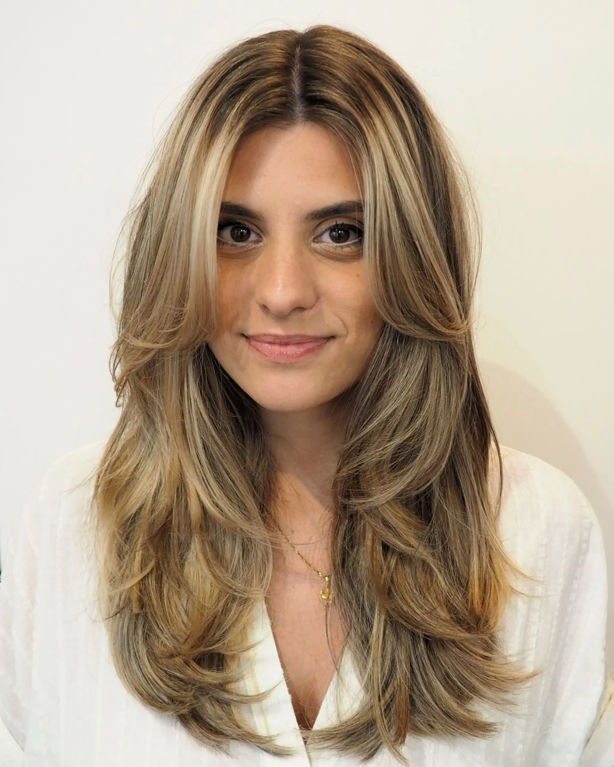 Long, wavy dark blonde hair with golden highlights, featuring a center part and face-framing layers.
