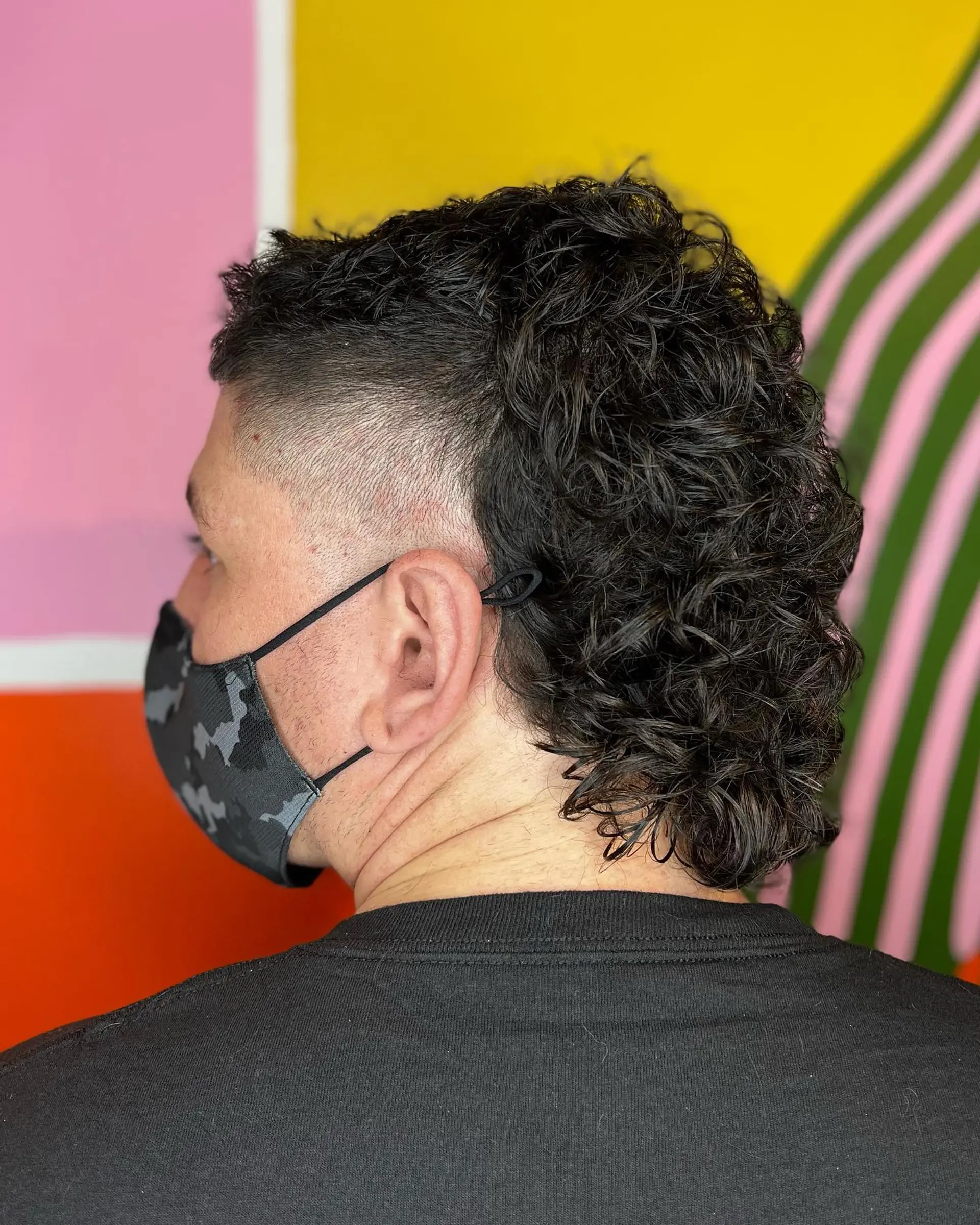 A modern curly mullet featuring a high fade on the sides with textured, defined curls cascading along the crown down to the nape. 1