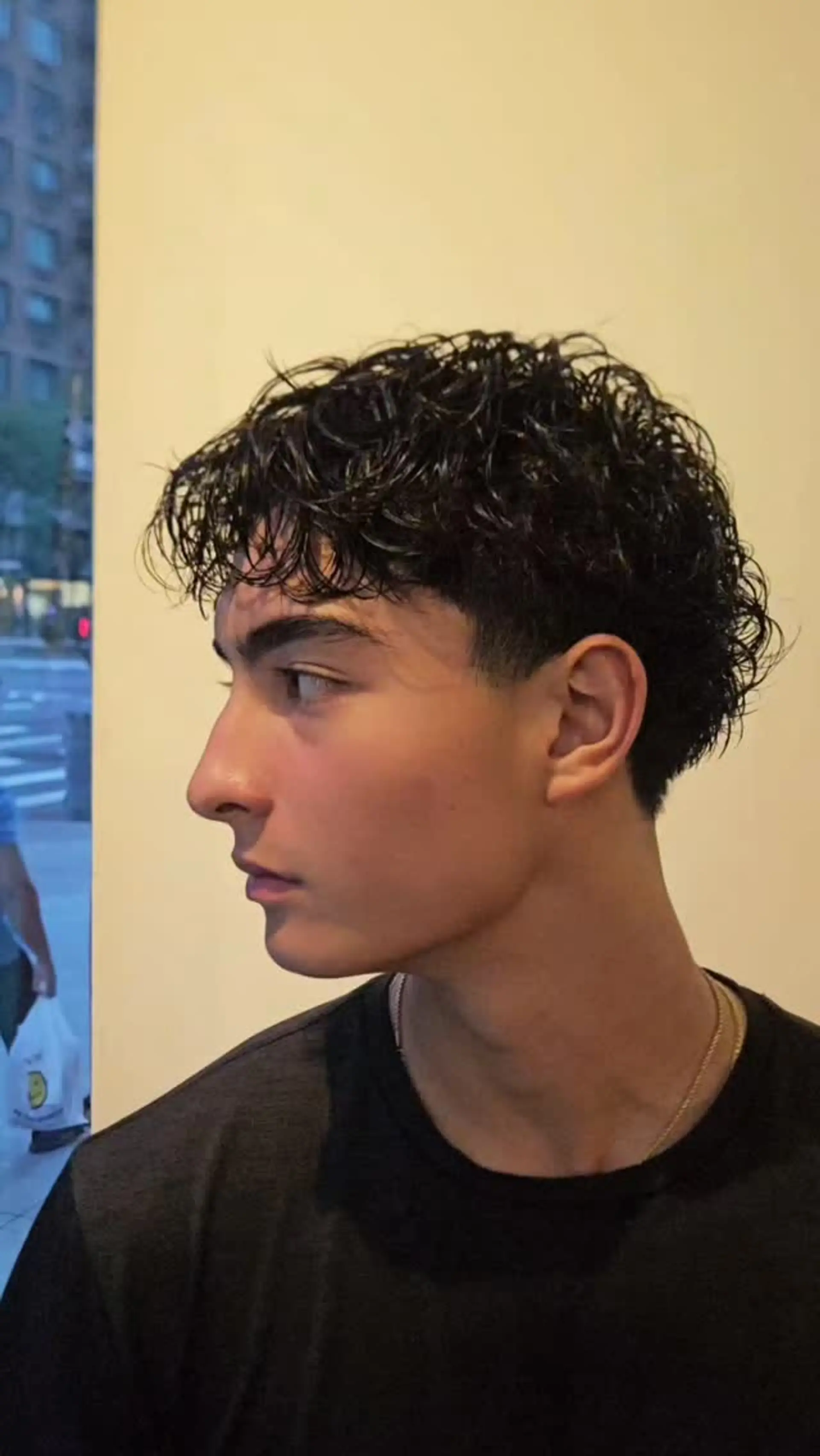 A short men's hairstyle featuring defined wet-look curls with a low taper fade around the temples and ears. 1