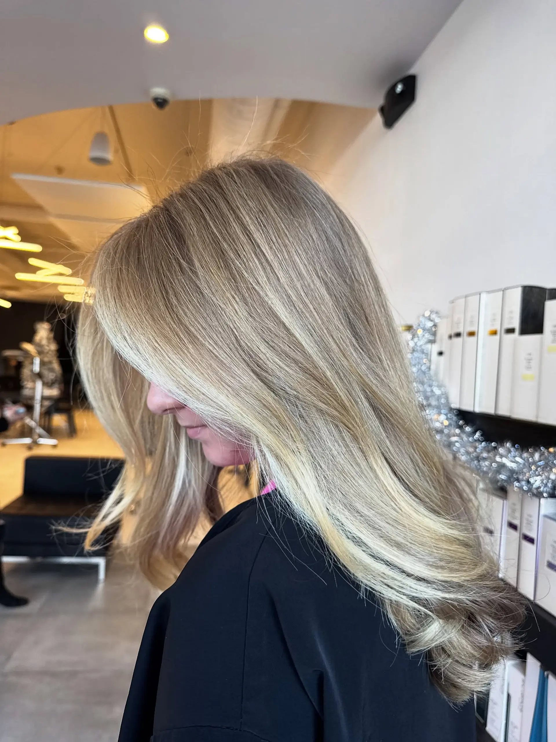 Side view of long, layered blonde hair styled in a smooth blowout with soft curved ends and bright face-framing pieces. 1