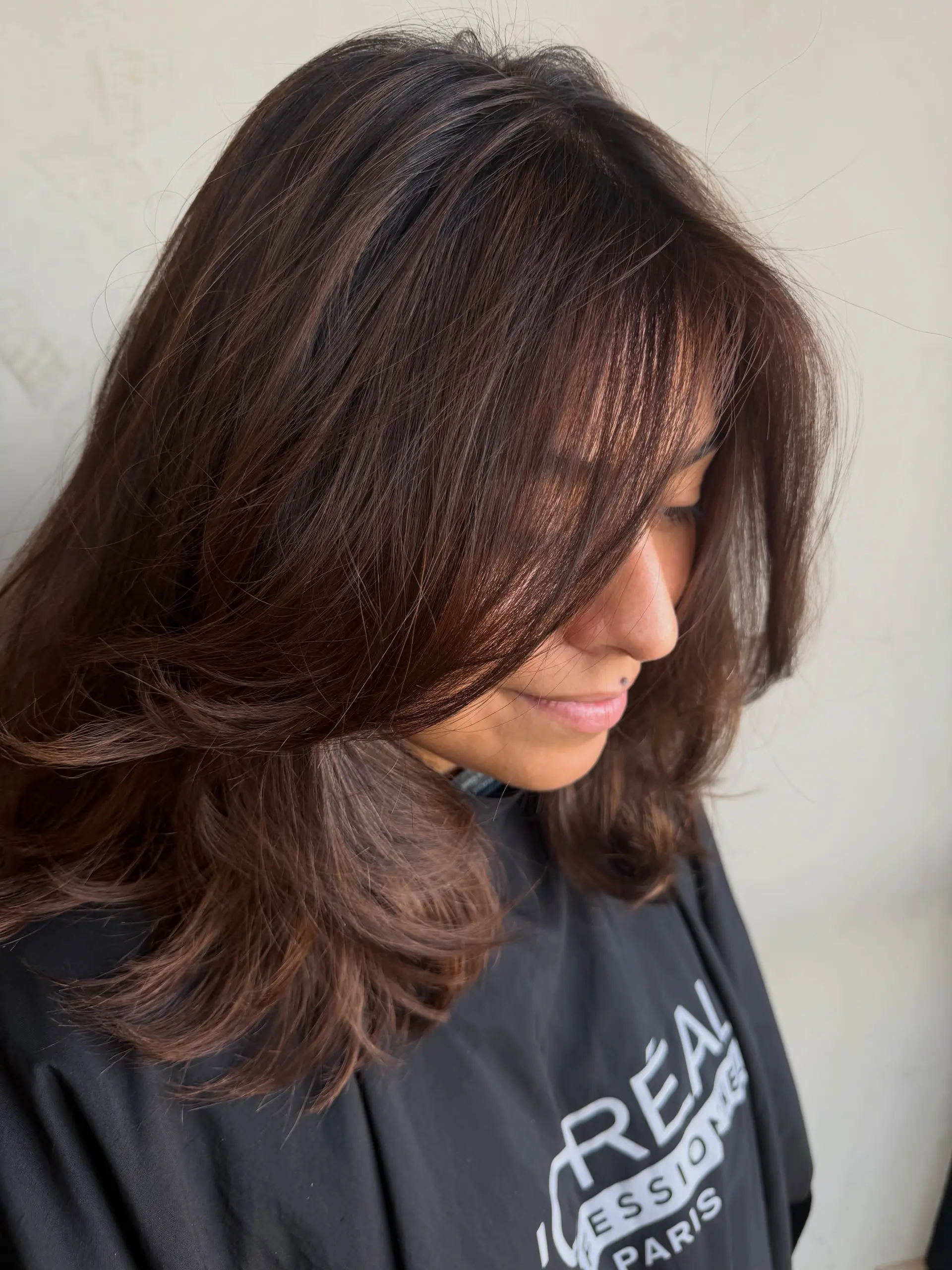 Medium-length layered rich brunette hair with soft dimensional tones and face-framing fringe styled with smooth, curled ends. 1