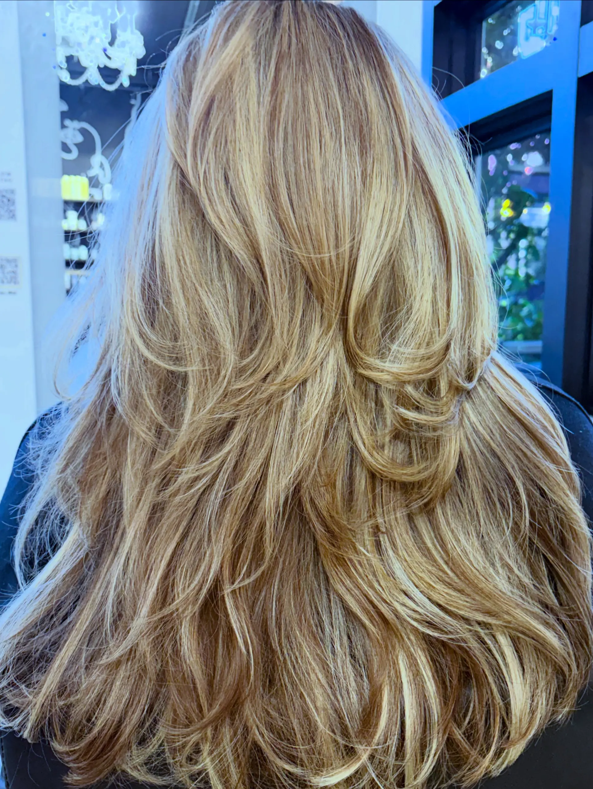Long dimensional golden blonde hair styled in feathered, cascading layers with soft flipped-under ends. 1