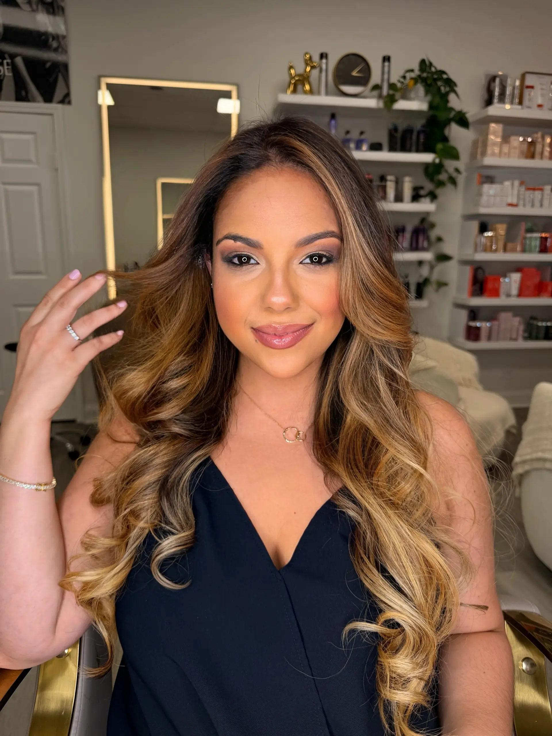 Long hair styled in polished, voluminous waves featuring a warm caramel and golden blonde dimensional balayage. 1