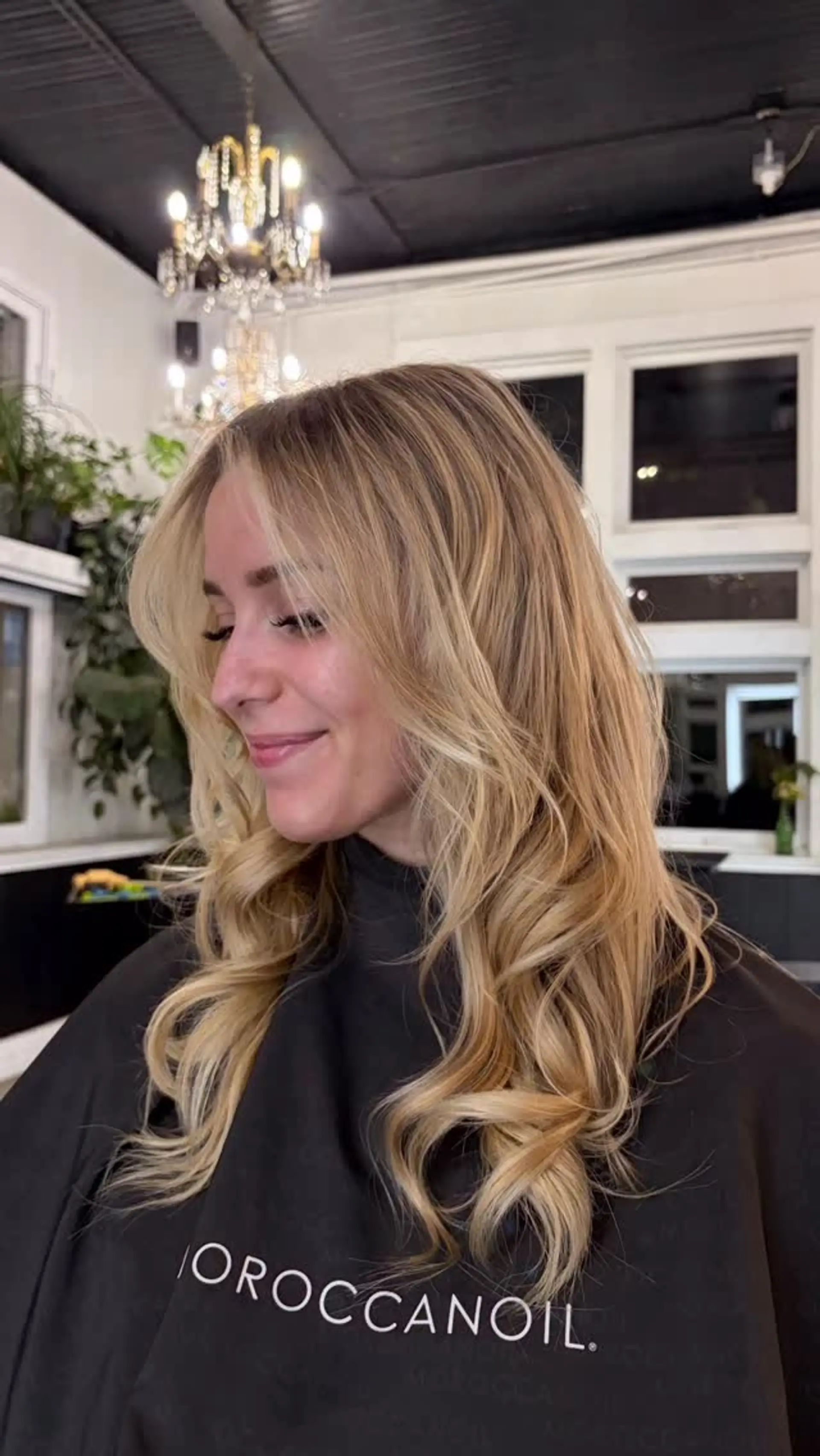 Long warm blonde hair styled into voluminous, loose curls with face-framing curtain bangs. 1