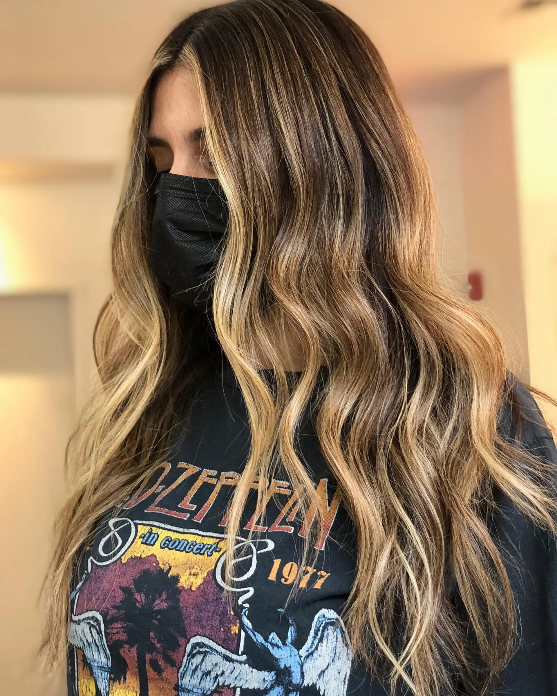 Long dark brown hair enhanced with seamless caramel and golden blonde babylights and balayage, styled into effortless loose waves. 1