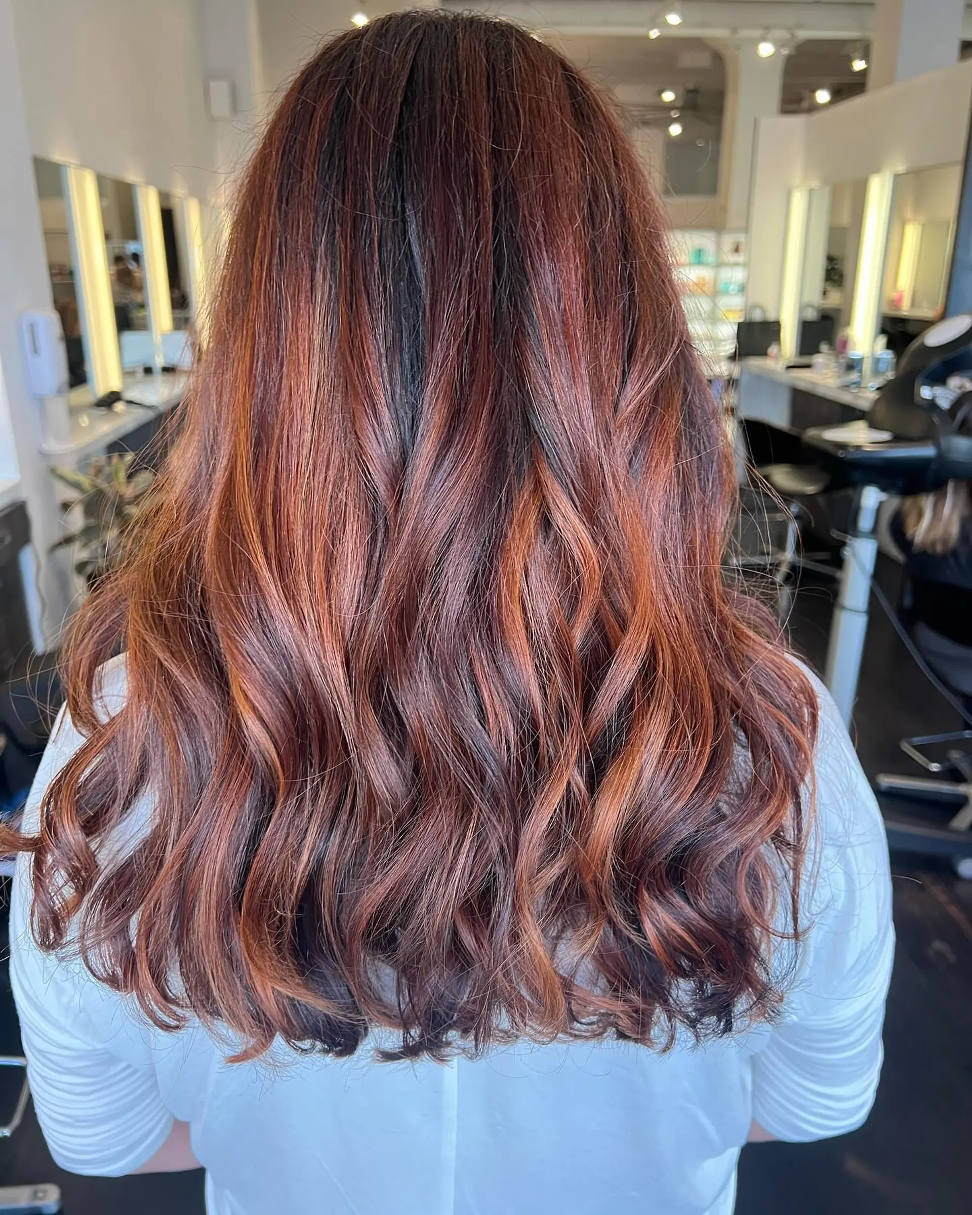 Long wavy hair with a vibrant copper and auburn balayage blended over a dark brunette base. 1