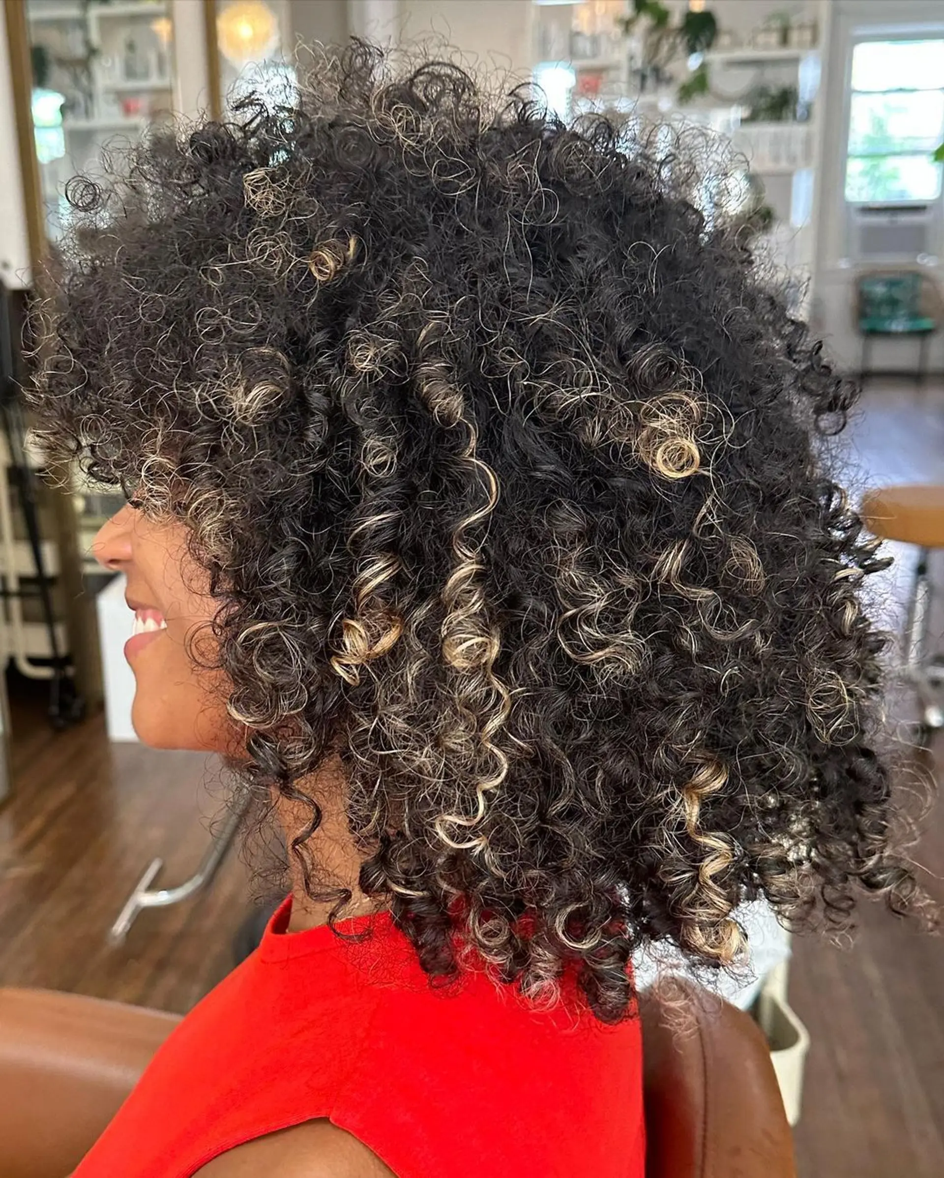 Voluminous, medium-length curly hair with black and blonde highlights with dynamic bounce. 2