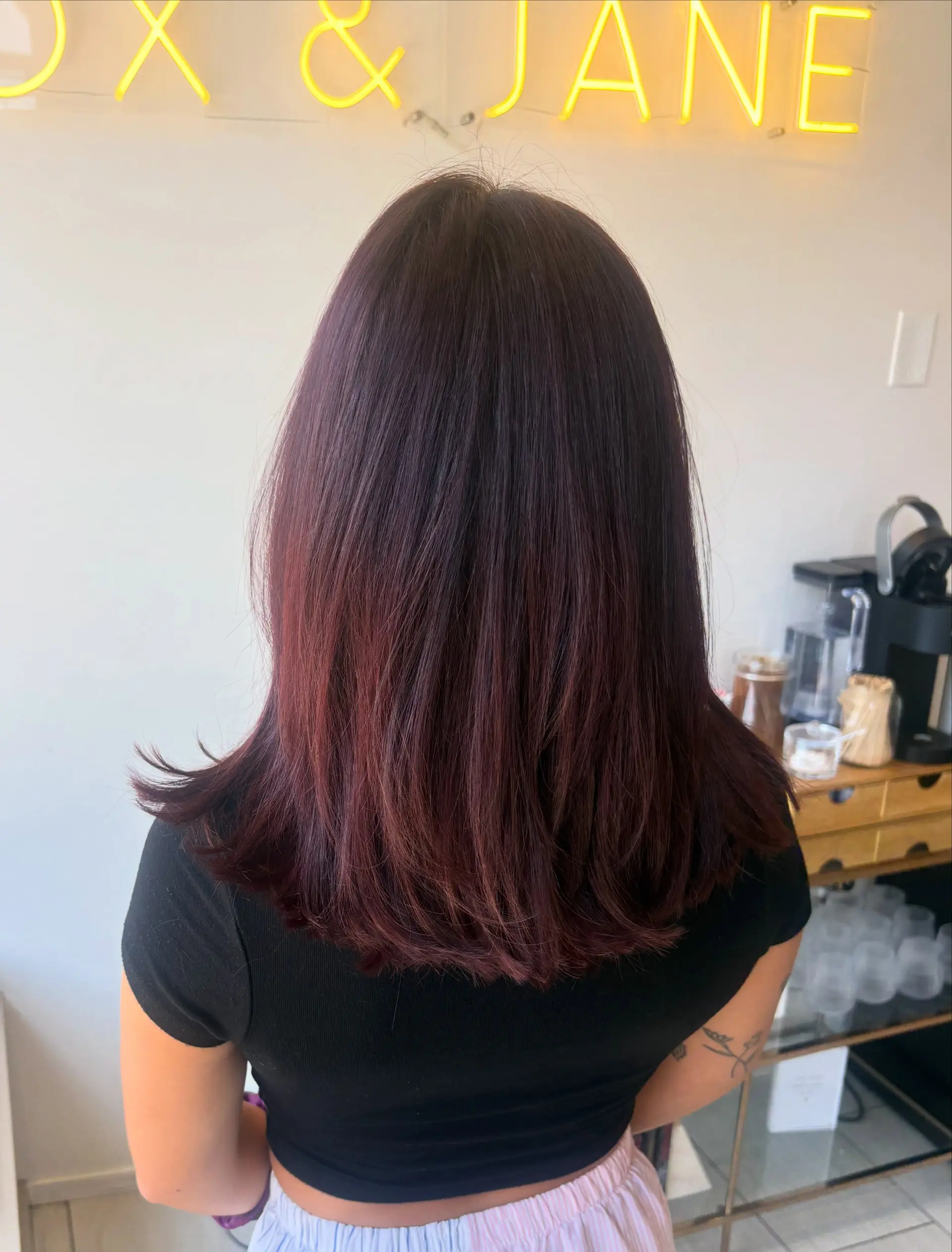 Medium-length layered haircut styled smooth and straight with softly flipped ends in a rich, dark burgundy tone. 1