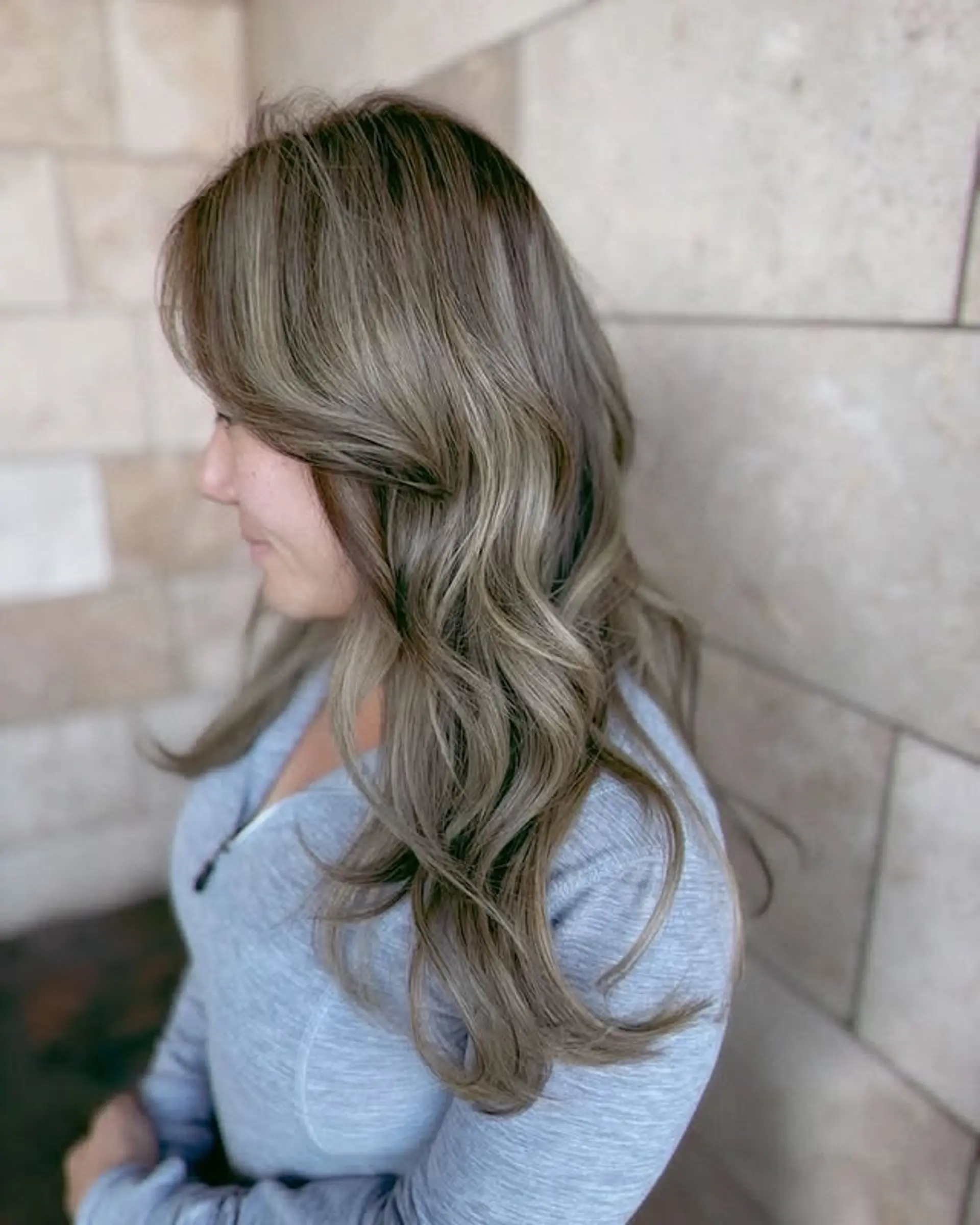 Long wavy hair with ash blonde balayage, curtain bangs, and face-framing layers. 1