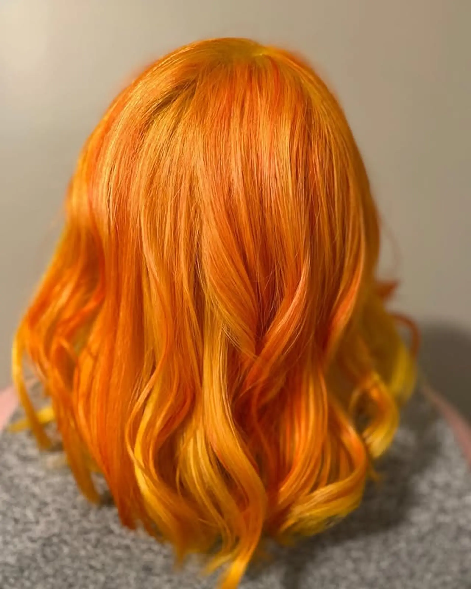 A vibrant ombre hairstyle with orange roots blending into yellow ends, styled into loose waves. 1