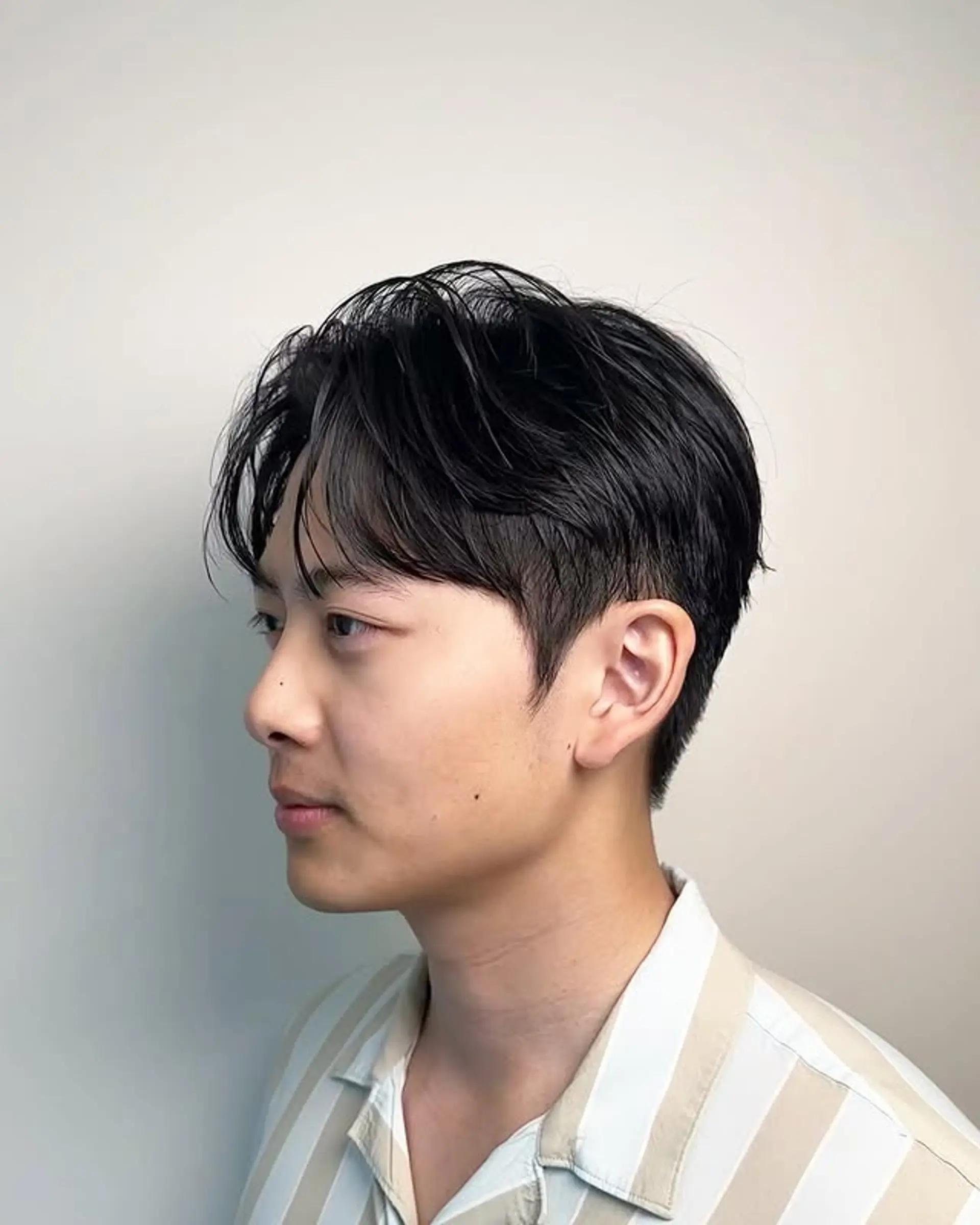 The hairstyle features soft waves on top with a clean taper fade on the sides and back. 1