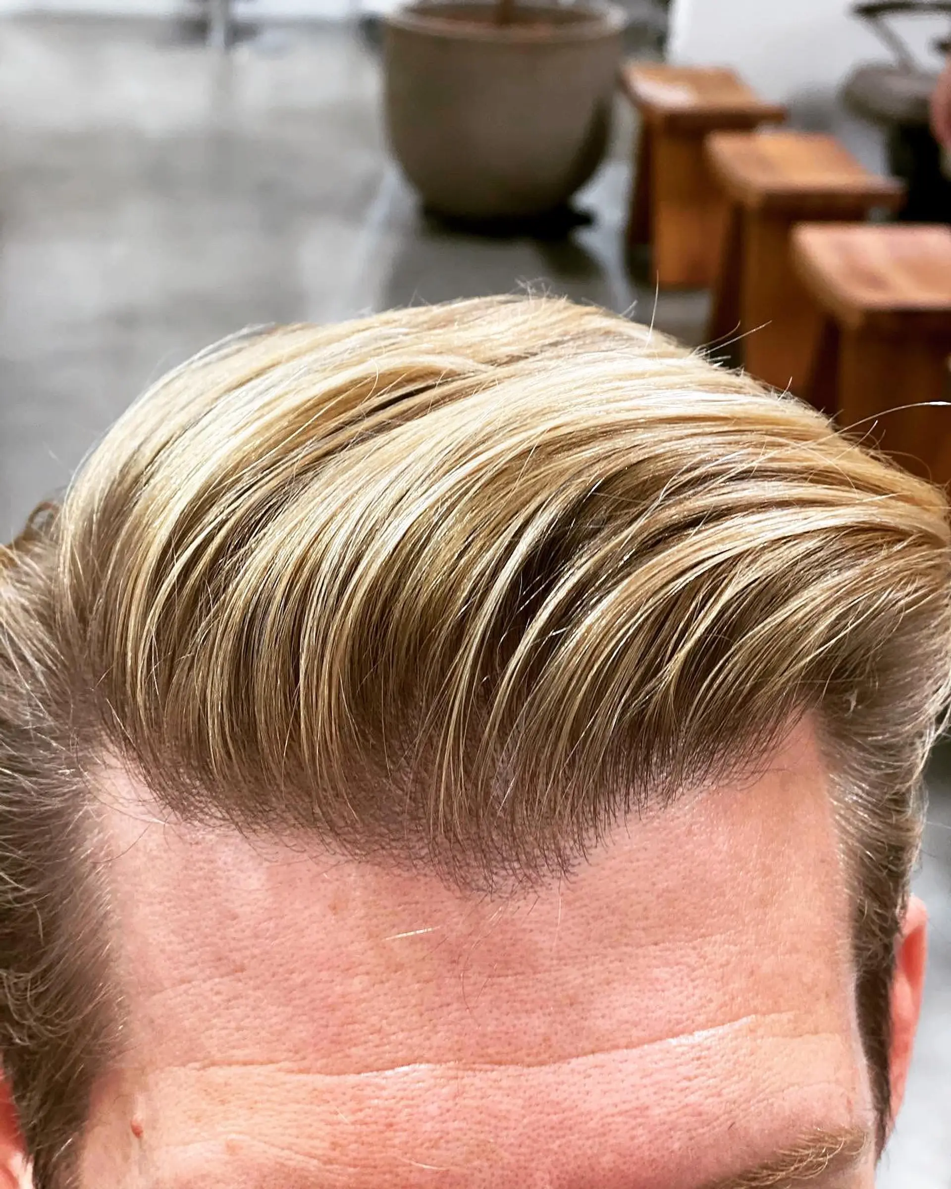 A sleek, swept-back men's hairstyle featuring fine, sun-kissed golden blonde balayage highlights seamlessly blended into darker blonde roots. 1