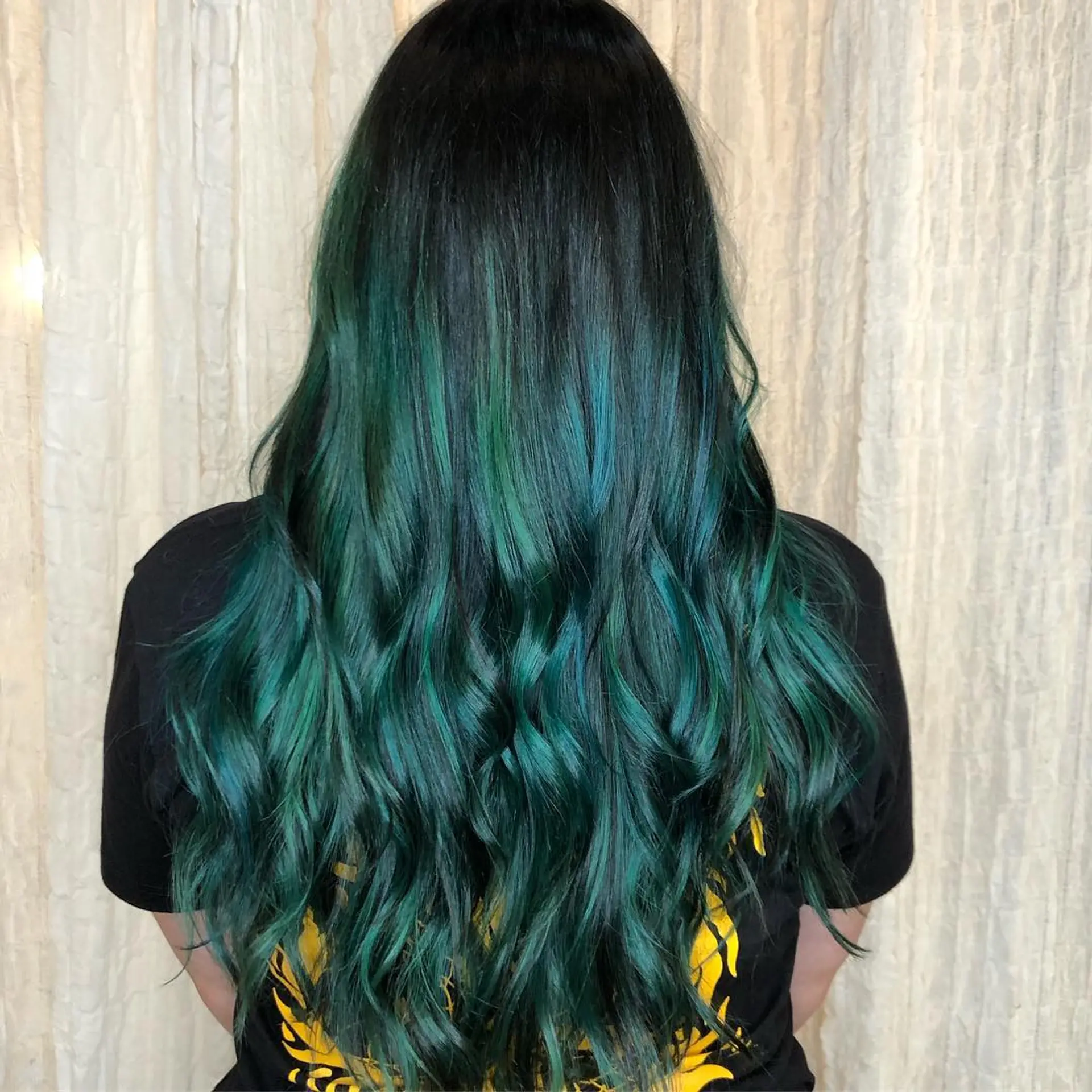 Long, dark hair featuring vivid emerald green balayage highlights styled in soft, cascading waves. 1