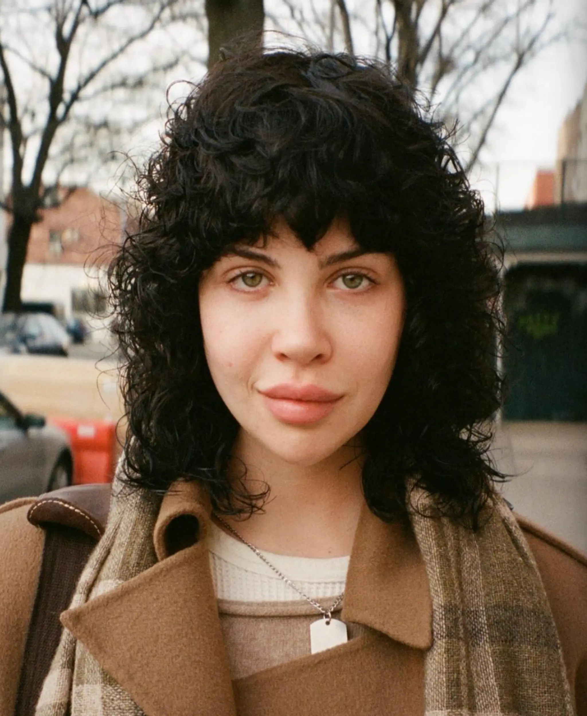 Medium-length black curly hair with voluminous curls, a full fringe, and layered, face-framing locks.