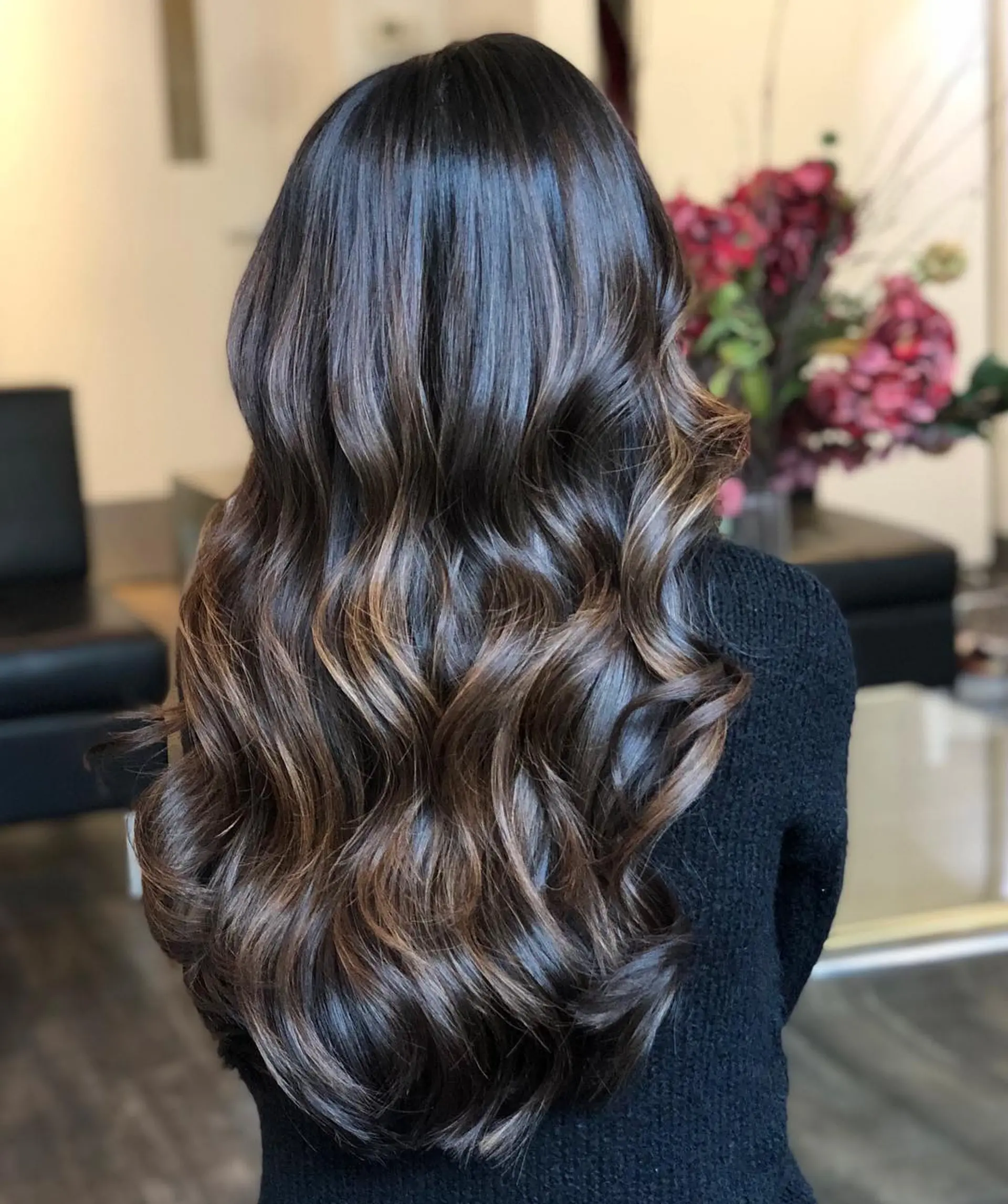 Long, glossy dark brown hair highlighted with subtle caramel balayage ribbons and styled into voluminous waves. 1