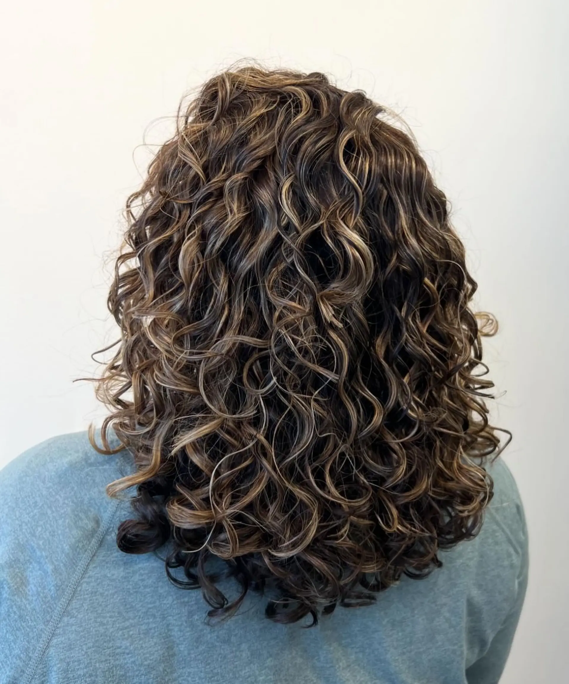 Medium-length defined curls featuring subtle caramel highlights and rounded layering for maximum volume and shape. 1