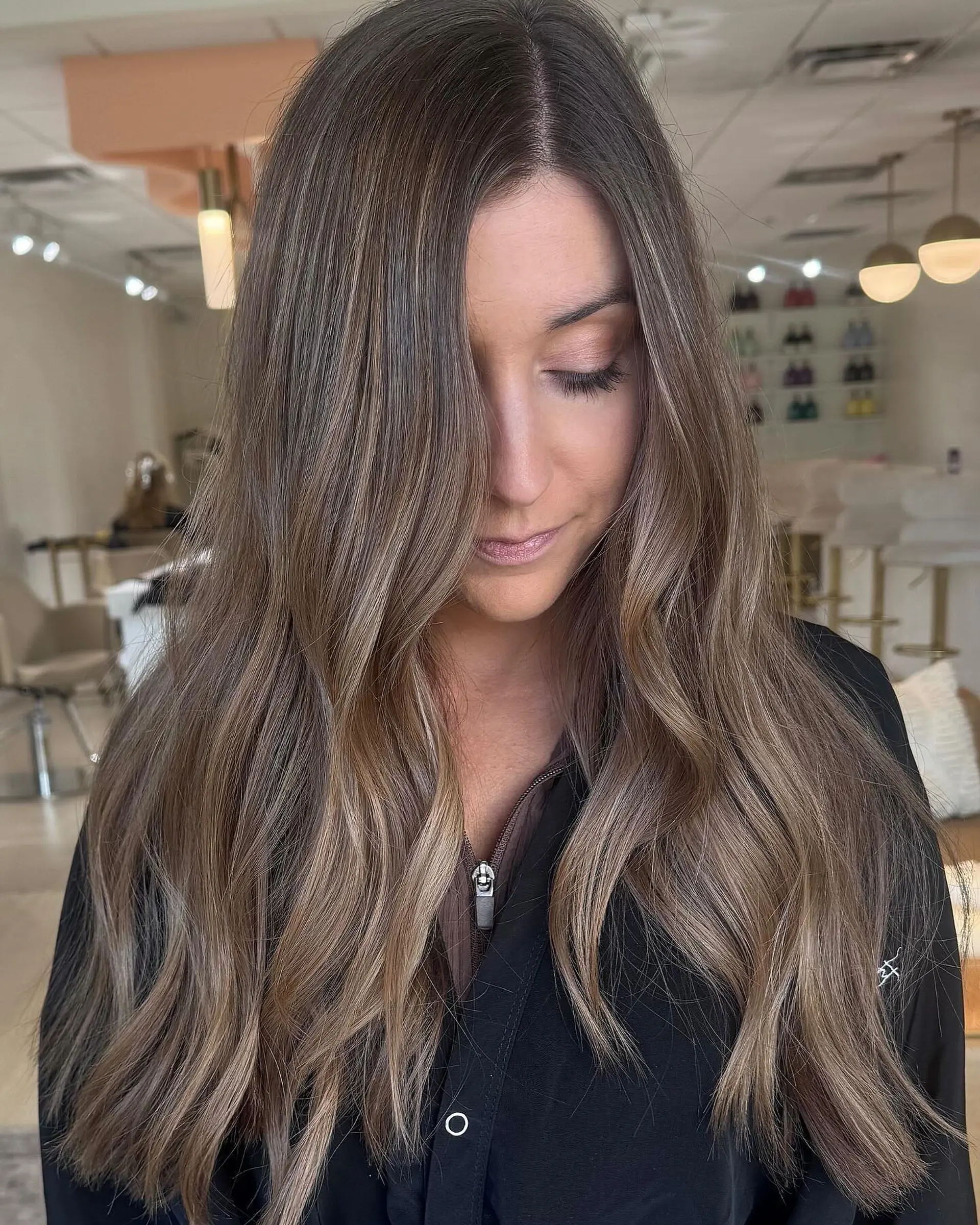 Long ash brunette hair detailed with soft, seamless balayage highlights and styled into loose waves. 1