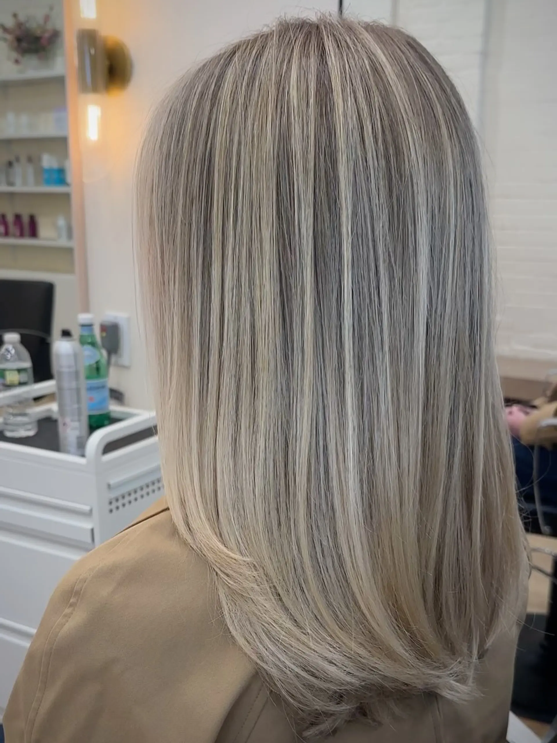 Sleek mid-length straight hair styled with subtle curved ends, featuring seamless dimensional cool blonde highlights. 1