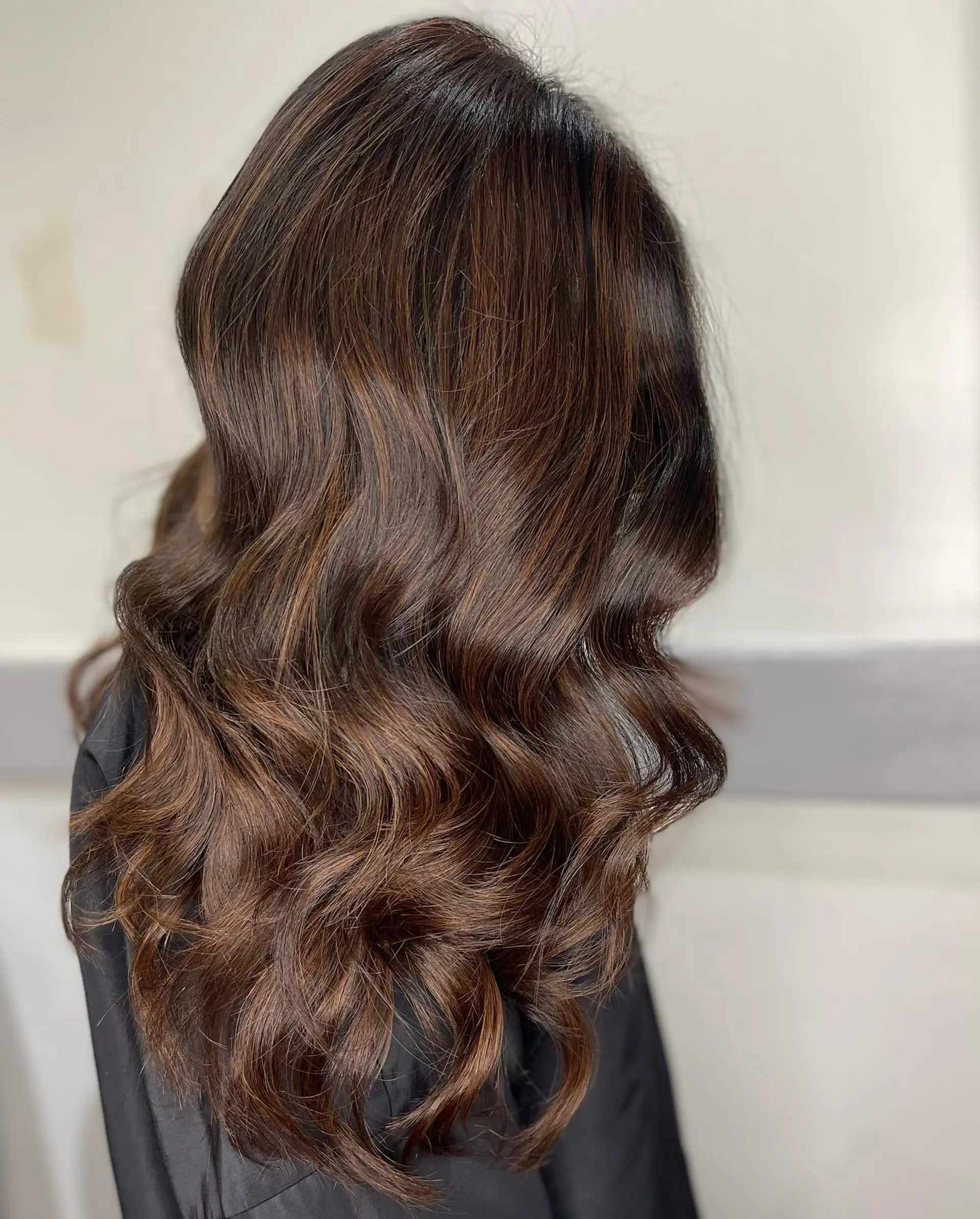 Long warm brunette hair styled into smooth, flowing waves with soft dimensional balayage highlights. 1
