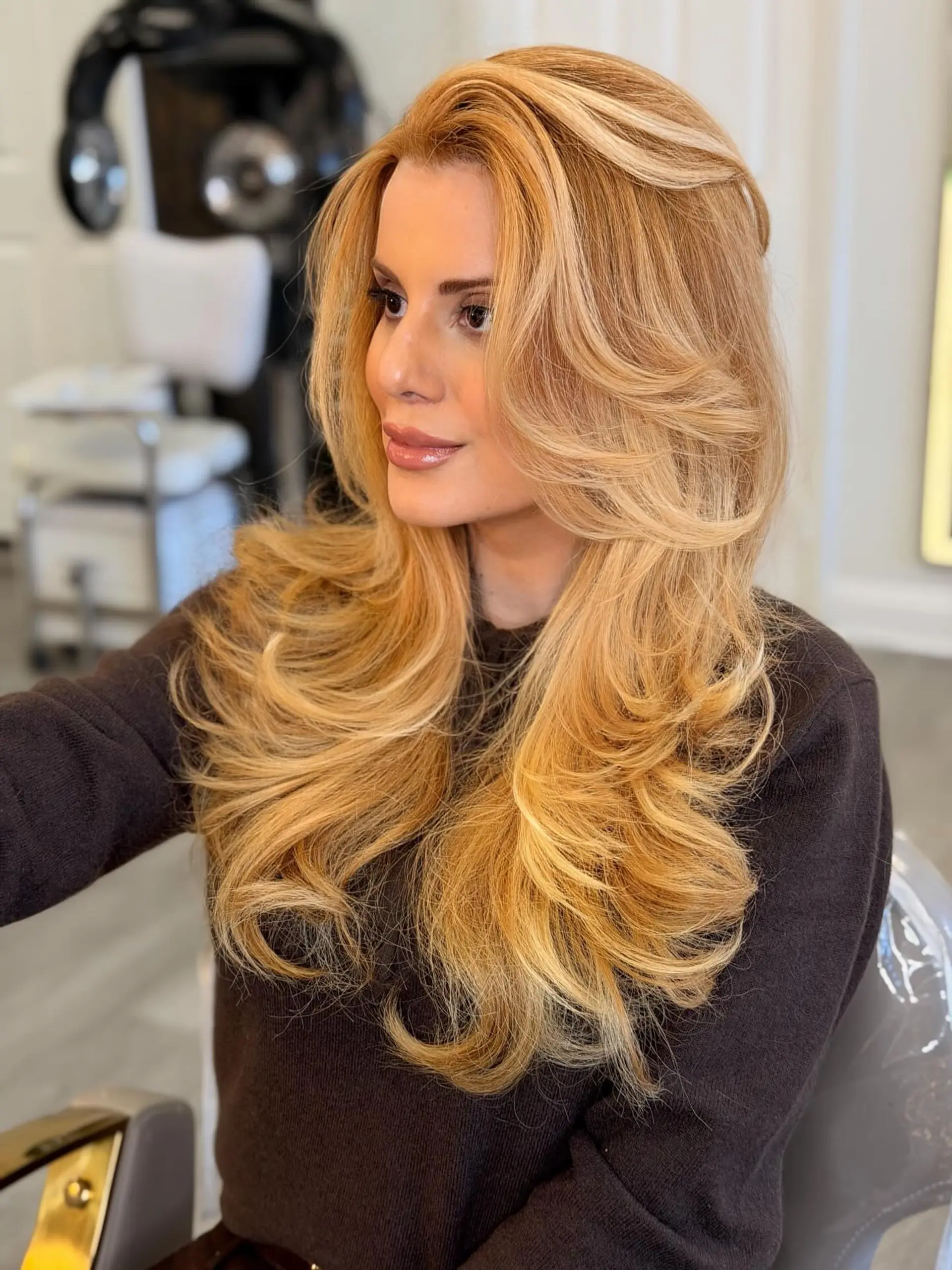 Long strawberry blonde hair featuring face-framing layers styled into a voluminous blowout with flipped ends. 1