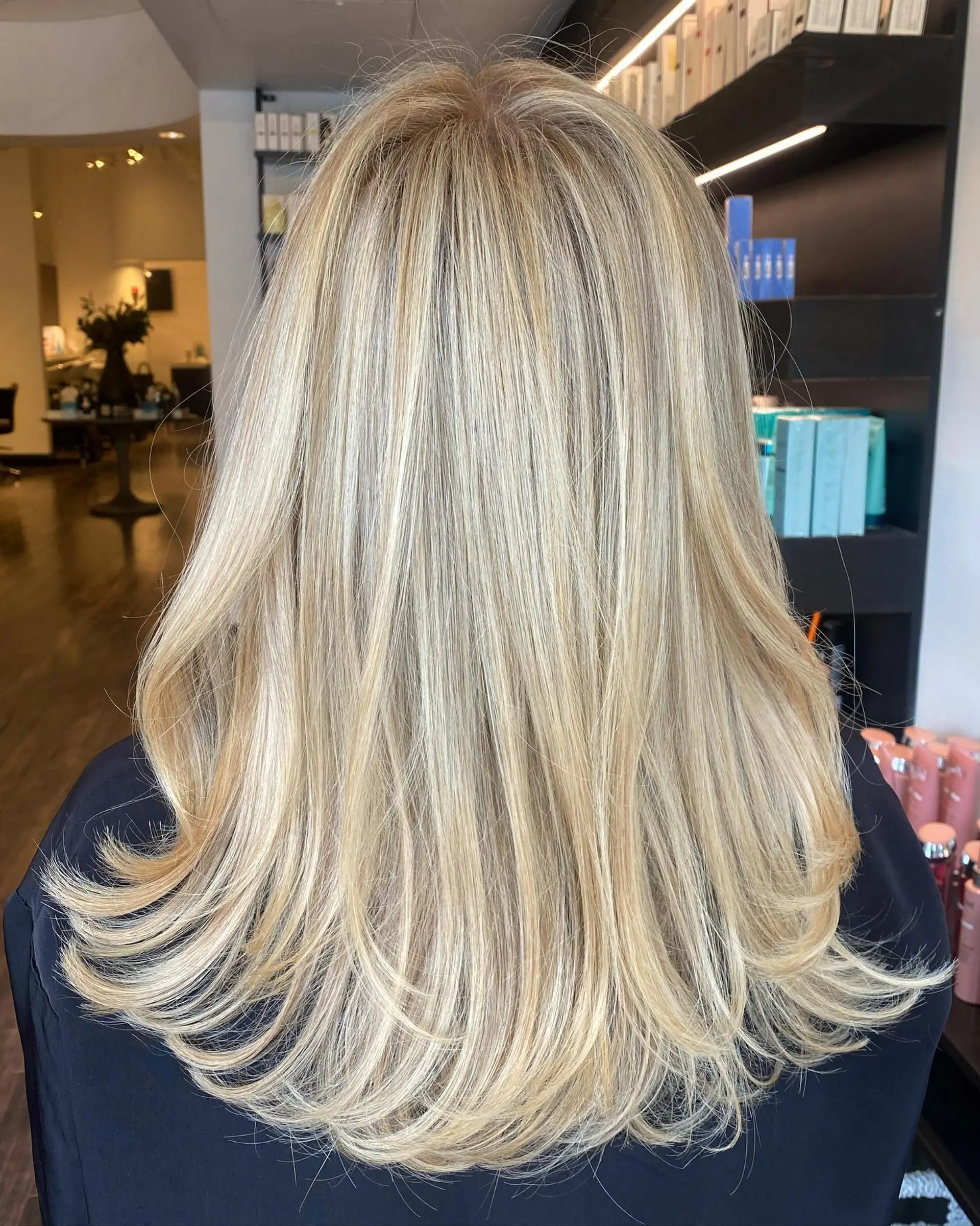 Long bright blonde hair styled in a smooth, layered blowout with soft flicked ends. 1