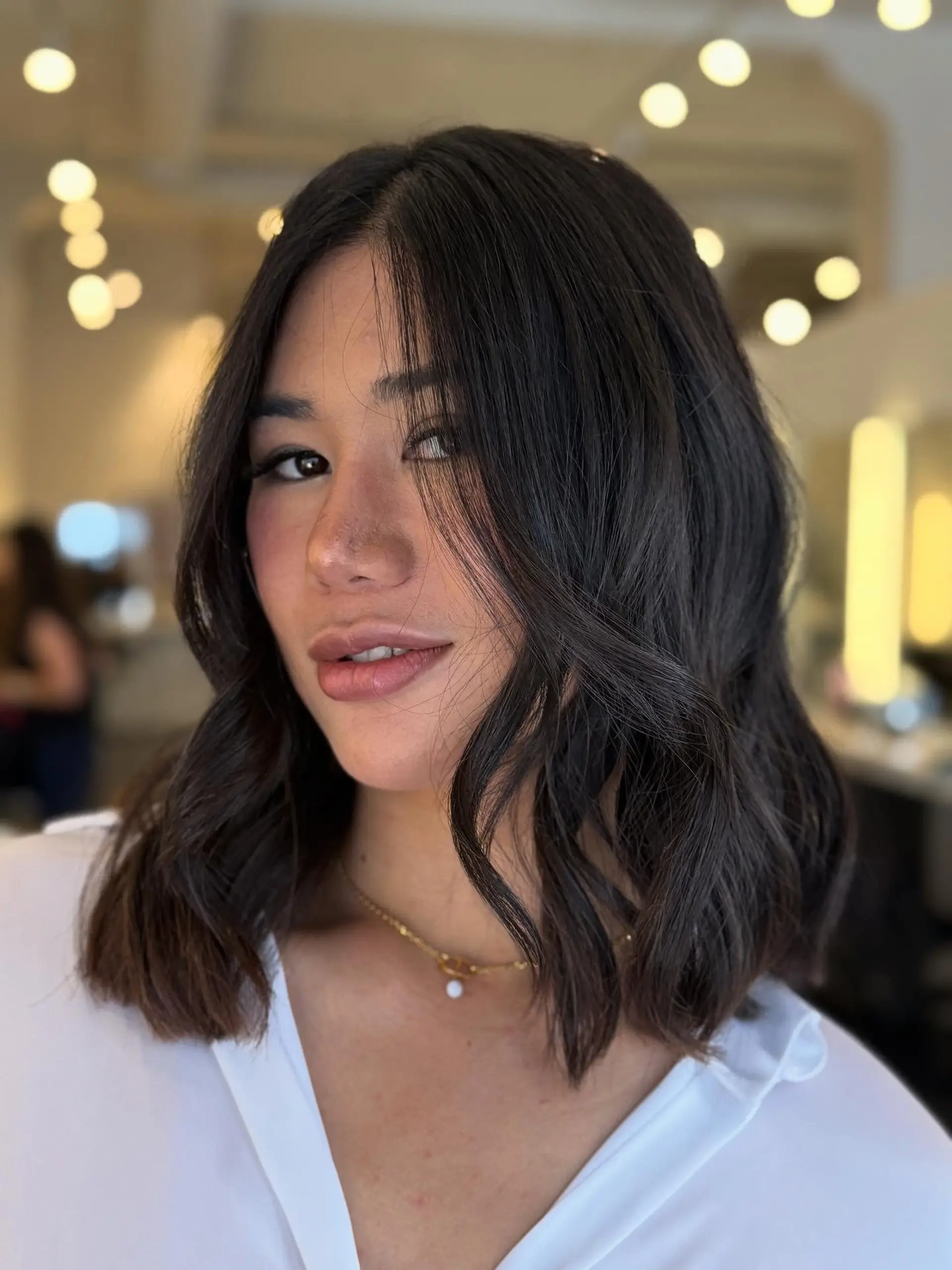A shoulder-length dark brown lob cut with subtle texture and styled into relaxed, soft waves with face-framing strands. 1