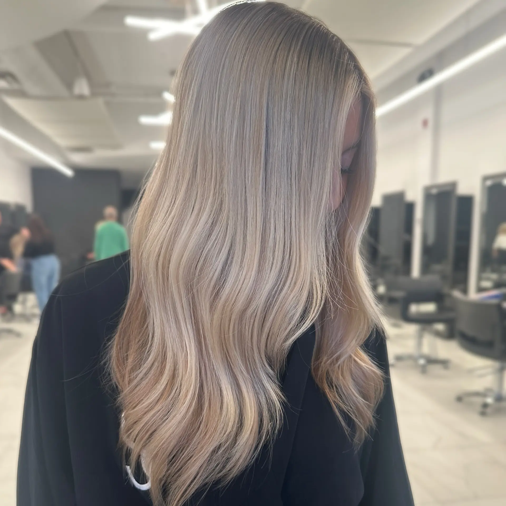 Long, dimensional ash blonde hair styled with smooth, cascading loose waves and a seamless root melt. 1