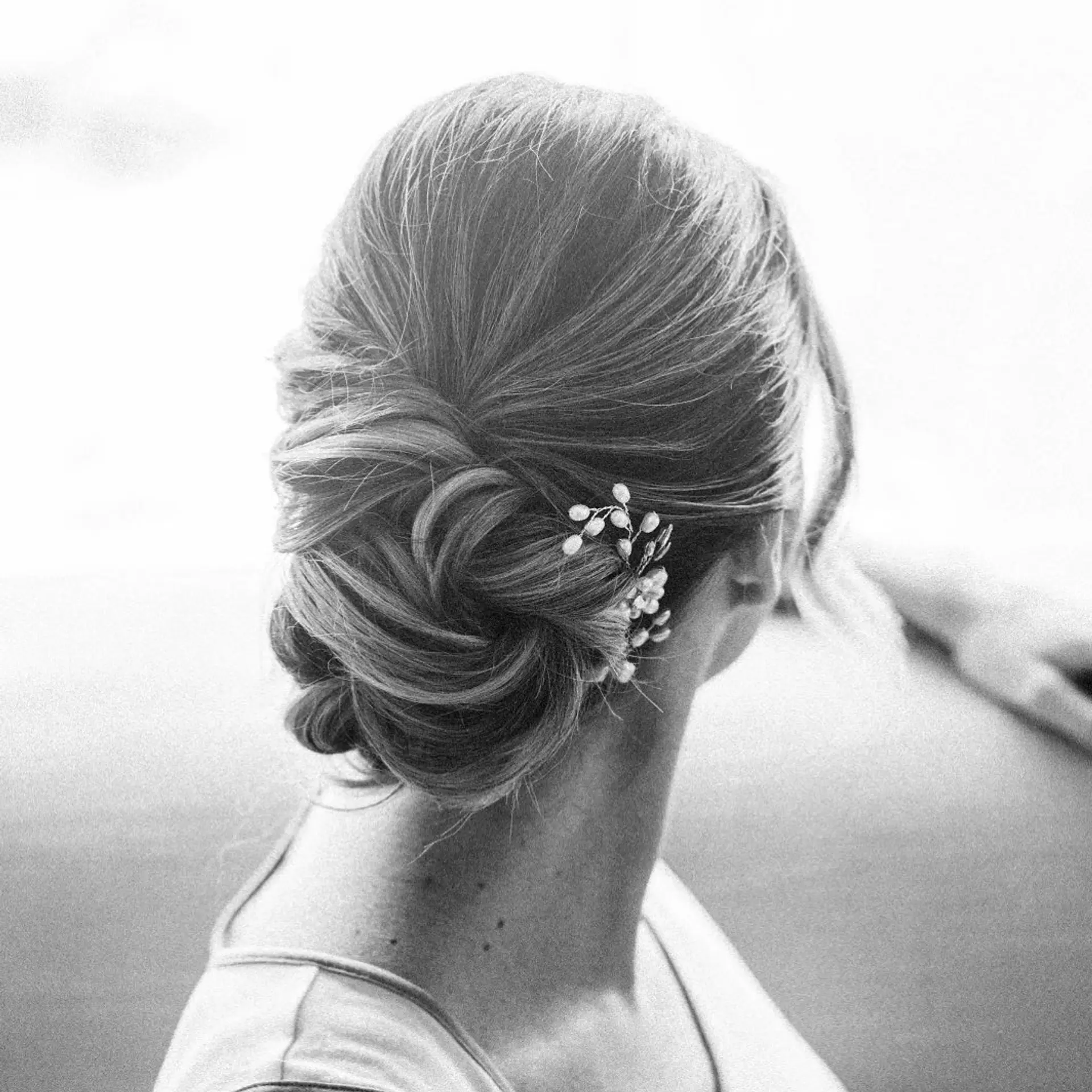 A romantic, textured low chignon updo tucked gracefully at the nape and accented with a delicate pearl hairpin. 1