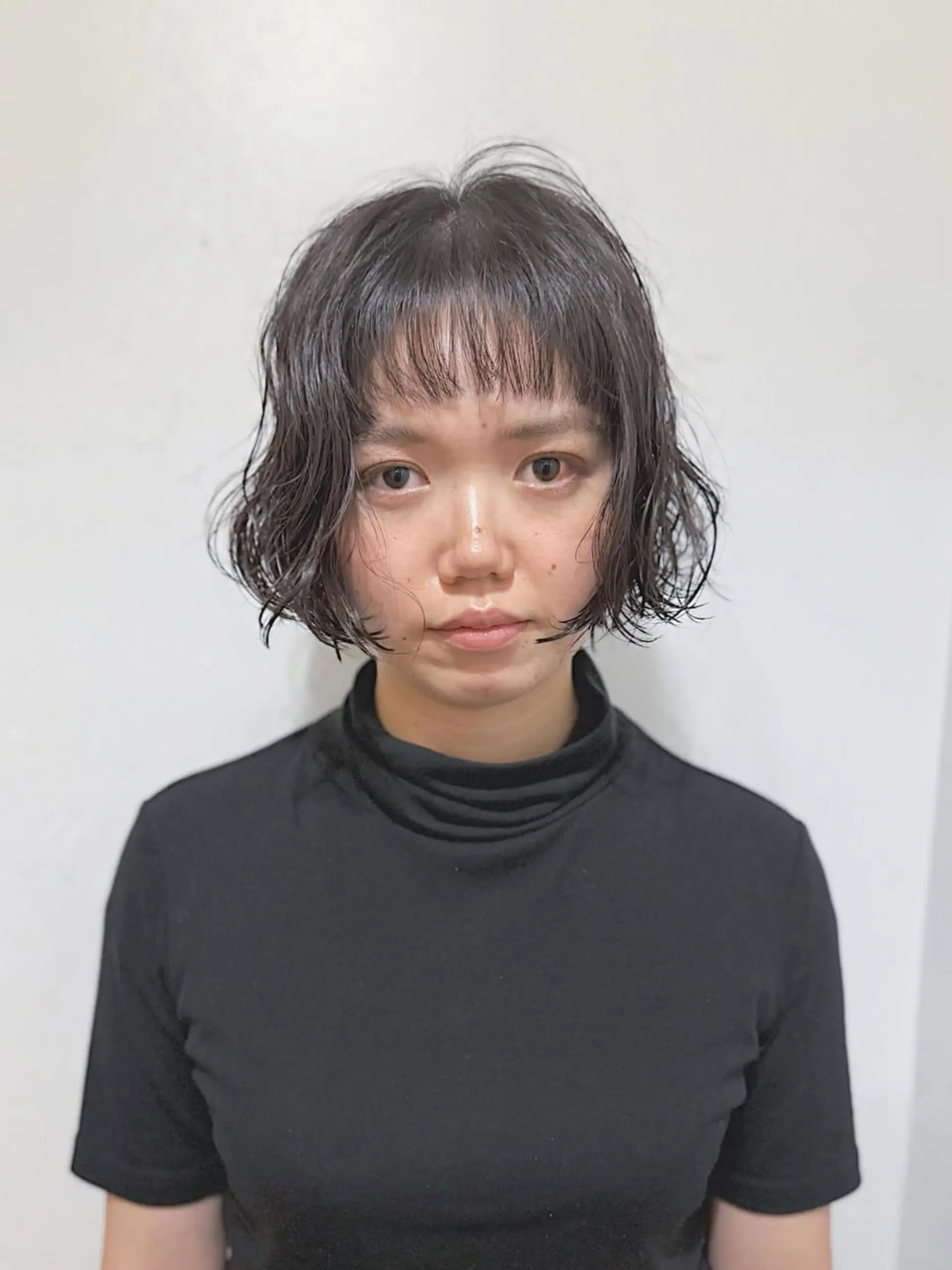A trendy short bob with a textured, wavy finish and eye-catching micro bangs. The hair is cut to jaw-length, creating a voluminous yet lightweight feel, perfect for a modern and stylish appearance. 1